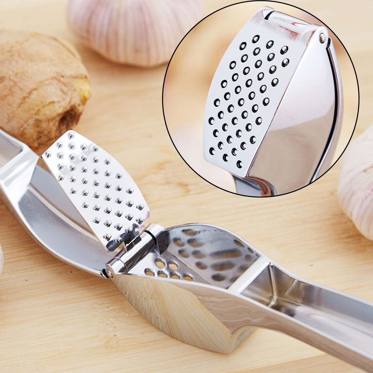 Eine Knoblauchpresse aus Metall auf einer Holzoberfläche. Im Hintergrund sind Knoblauchzehen und Ingwer zu sehen. Nahaufnahme.
