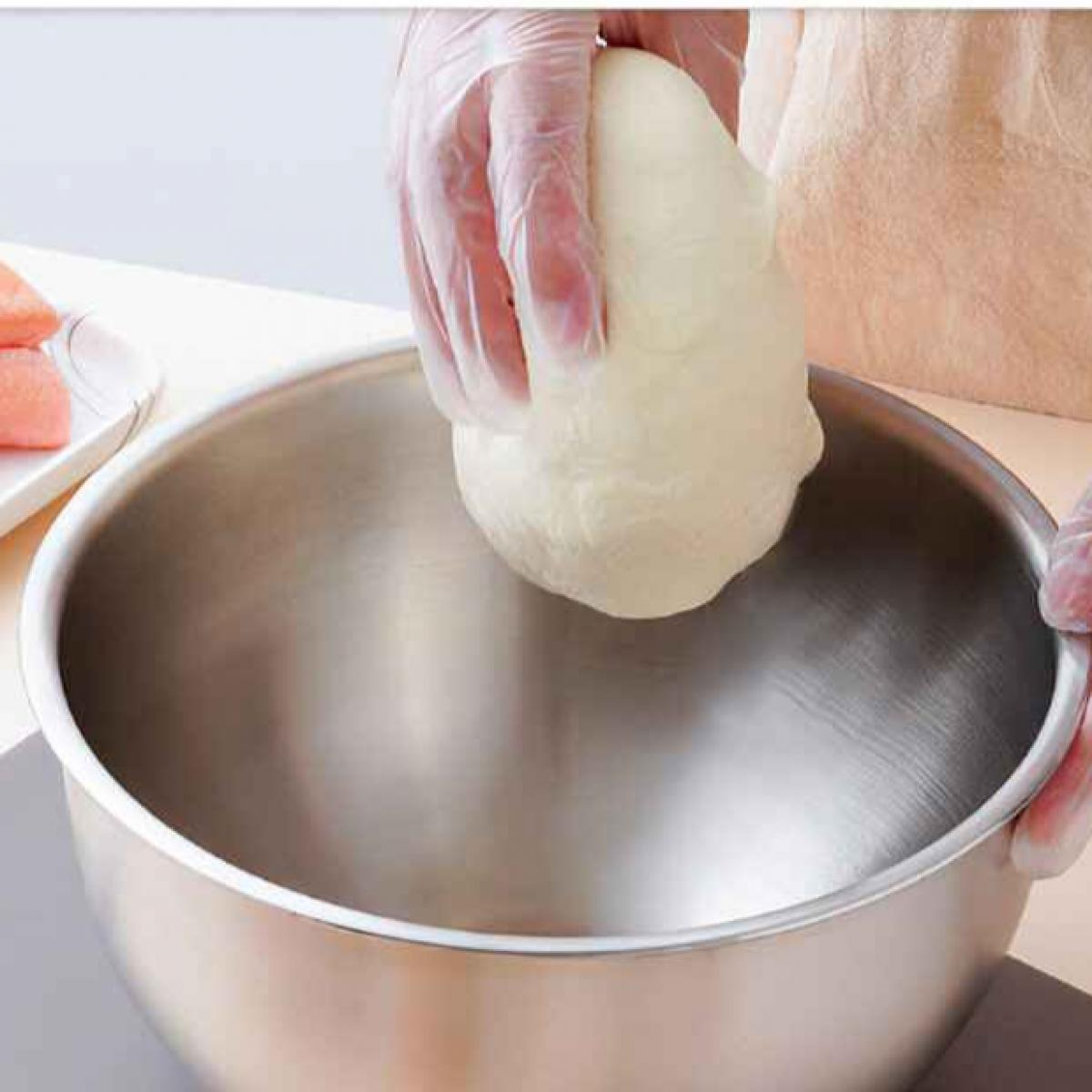 Hände in Handschuhen halten einen Teigball über einer Edelstahlschüssel. Links ein Teller mit rotem Essen.