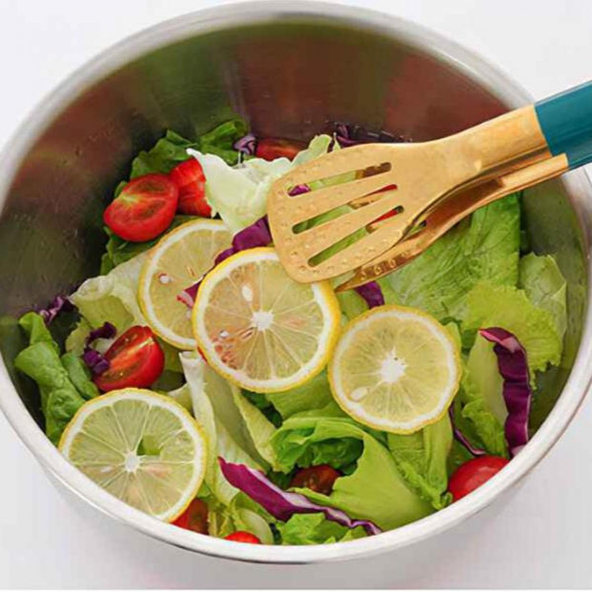 Eine Metallschüssel mit Salat, Zitronenscheiben und Tomaten. Zangen mit türkisfarbenen Griffen liegen obenauf.