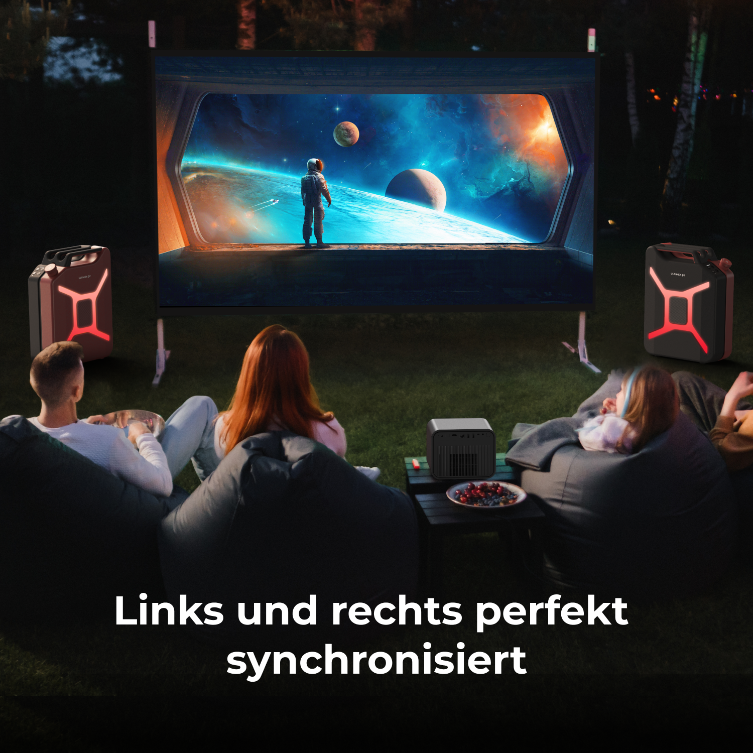 Leute schauen im Garten einen Film. Ein Bildschirm zeigt eine Weltraumszene. Lautsprecher sind an den Seiten. Text: 'Links und rechts perfekt synchronisiert'.