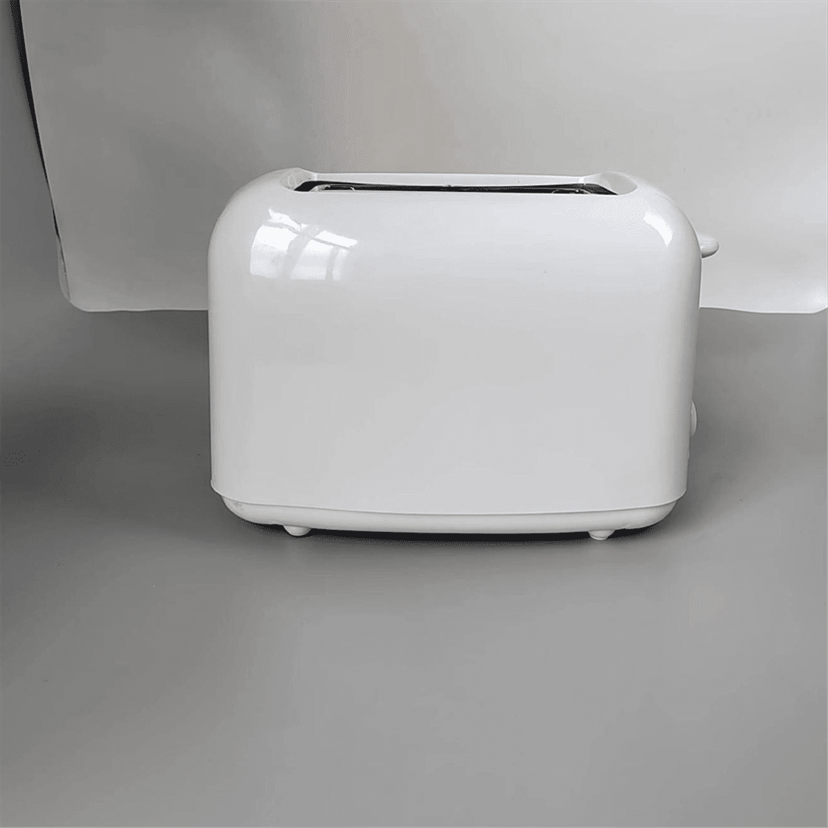 Ein weißer Toaster auf grauem Untergrund. Er hat ein abgerundetes Design mit Schlitzen oben. Der Hintergrund ist hellgrau.