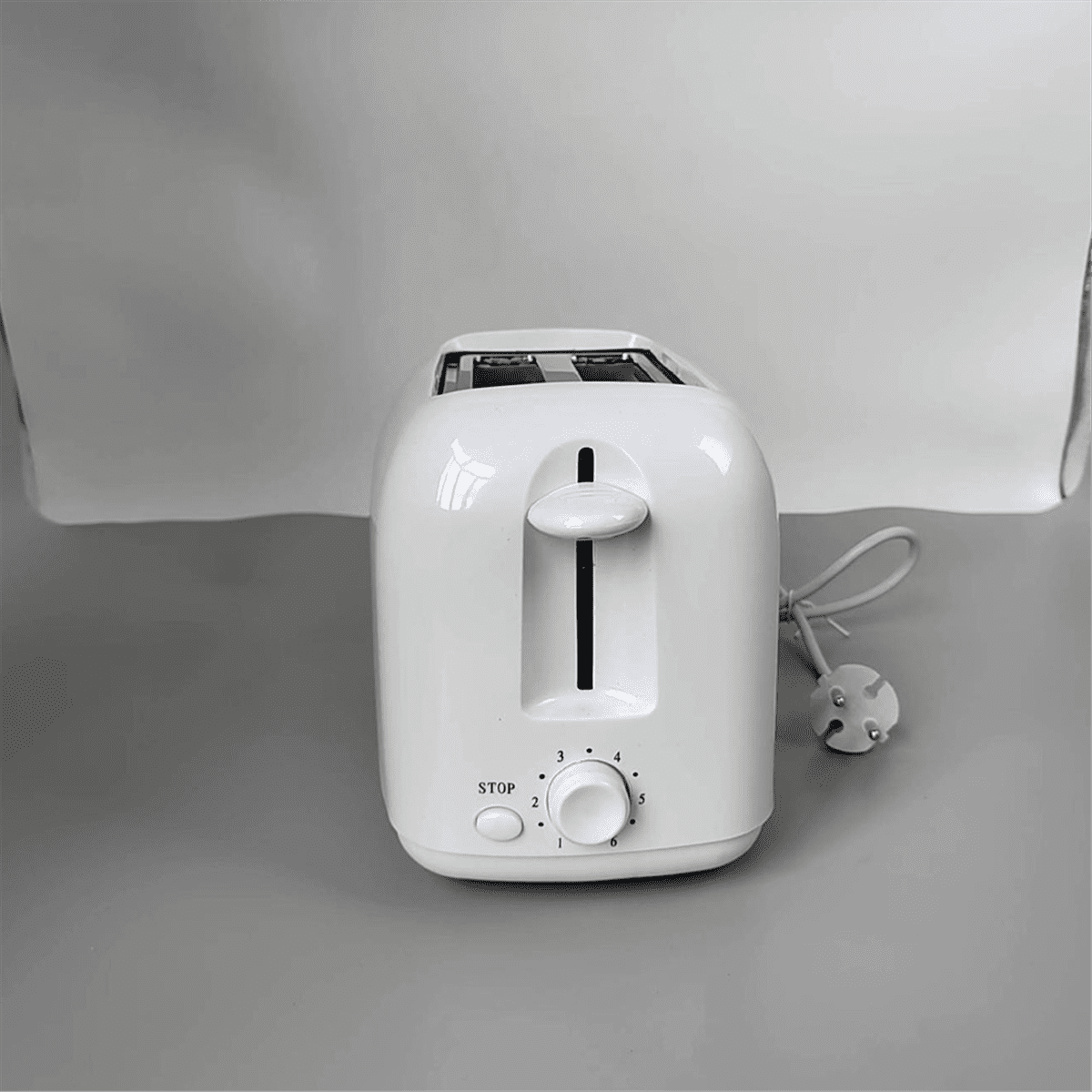 Ein weißer Toaster mit Drehknopf und Stopptaste. Stecker und Kabel sind angeschlossen. Der Hintergrund ist hellgrau.