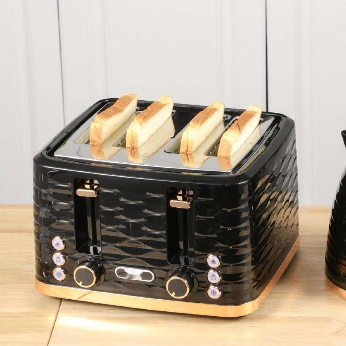 Ein schwarz-goldener Toaster mit vier Brotscheiben. Er steht auf einer Holzoberfläche, im Hintergrund eine weiße Wand.