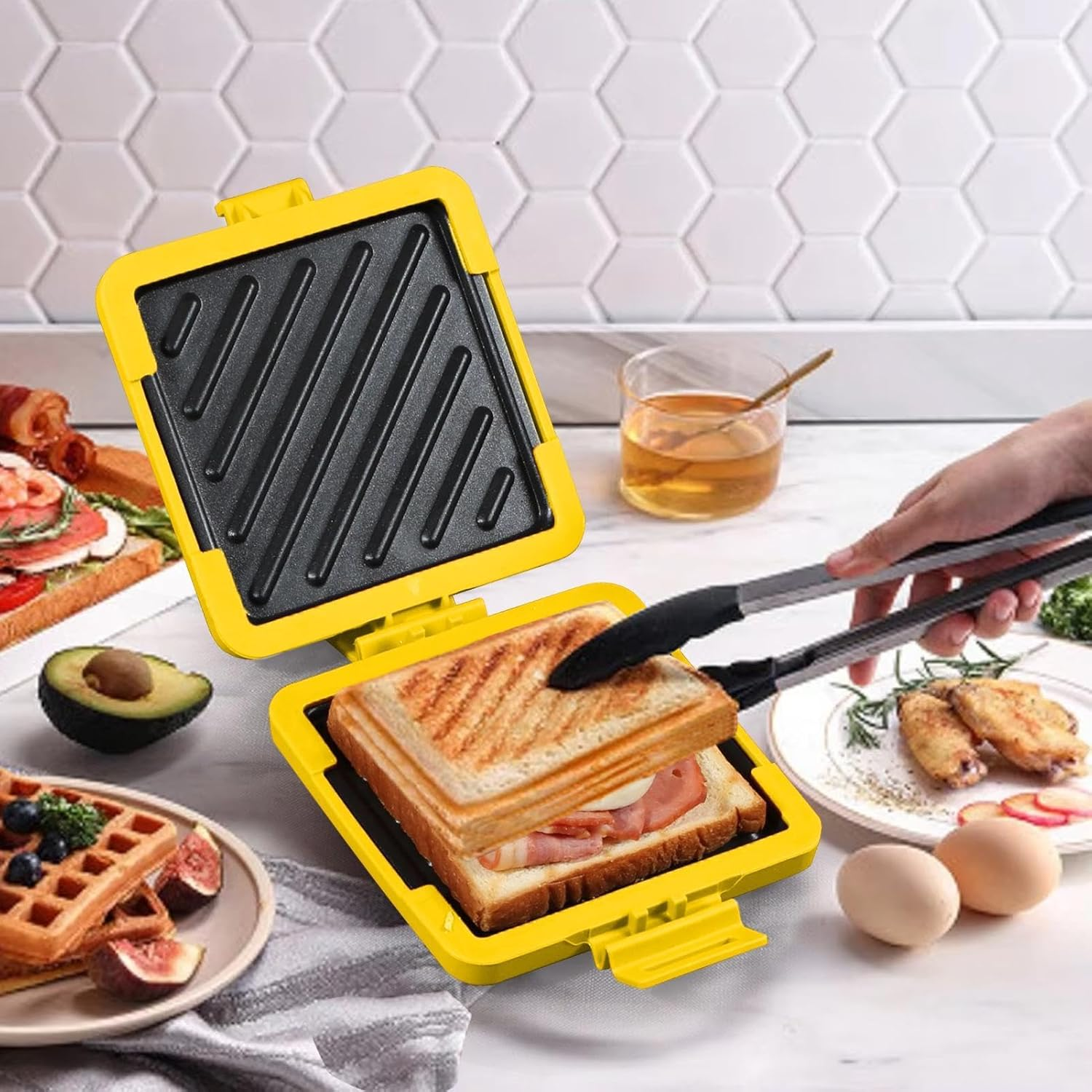 Ein gelber Sandwichmaker mit einem gegrillten Sandwich. Andere Lebensmittel wie Waffeln, Eier und Wings sind dabei.
