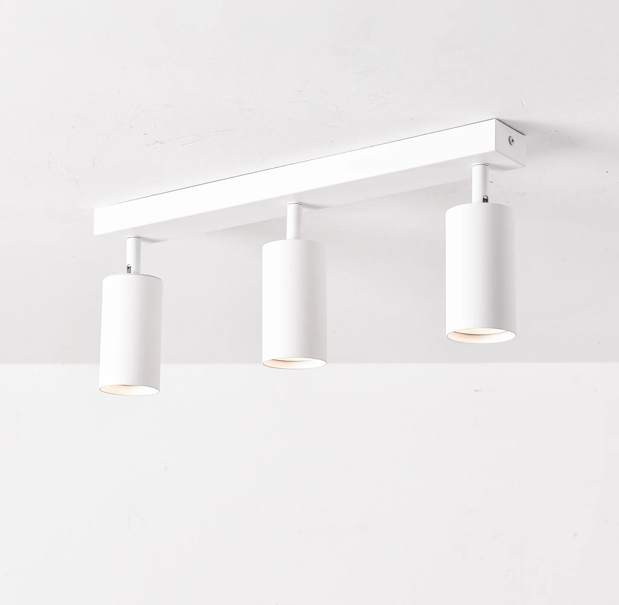 Eine weiße Deckenleuchte mit drei zylindrischen Strahlern vor weißem Hintergrund. Jede Lampe leuchtet.