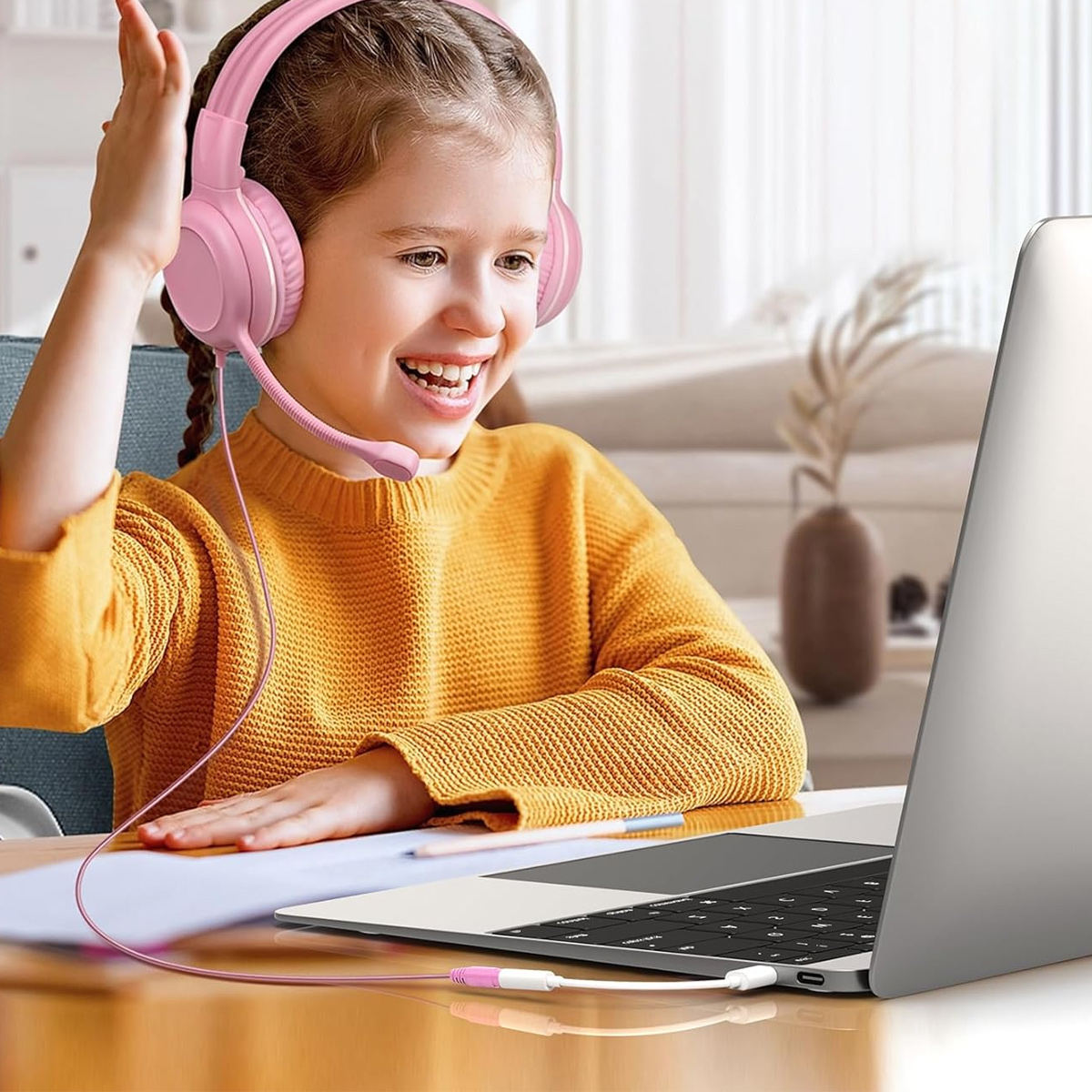 Ein Mädchen mit rosa Kopfhörern lächelt auf einen Laptop. Sie trägt einen gelben Pullover. Ein Kabel verbindet die Kopfhörer mit dem Laptop.