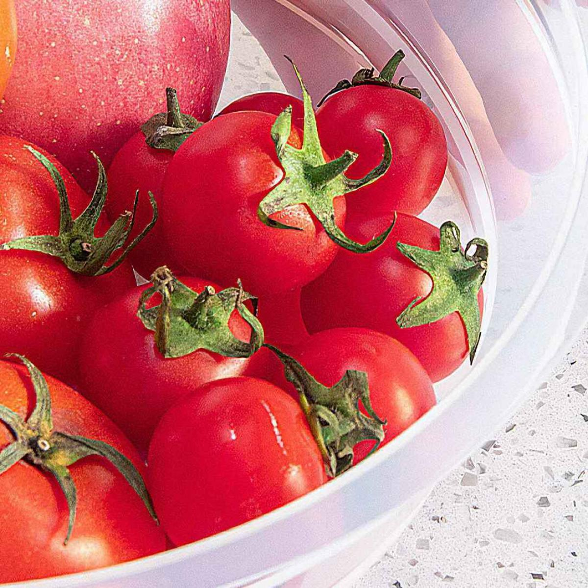 Nahaufnahme von roten Cherrytomaten mit grünen Stielen in einer weißen Schüssel, mit einem roten Apfel im Hintergrund.
