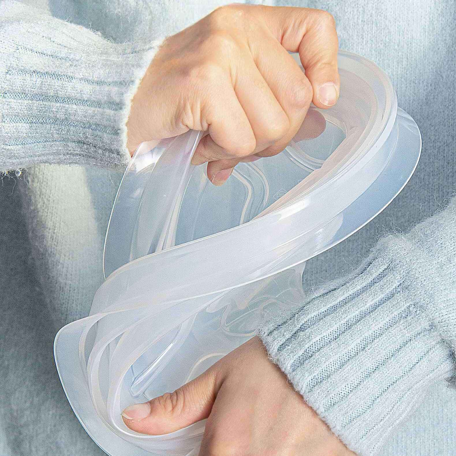 Hände halten einen durchsichtigen, flexiblen Behälter vor einem hellblauen Pullover. Der Behälter ist kreisförmig.