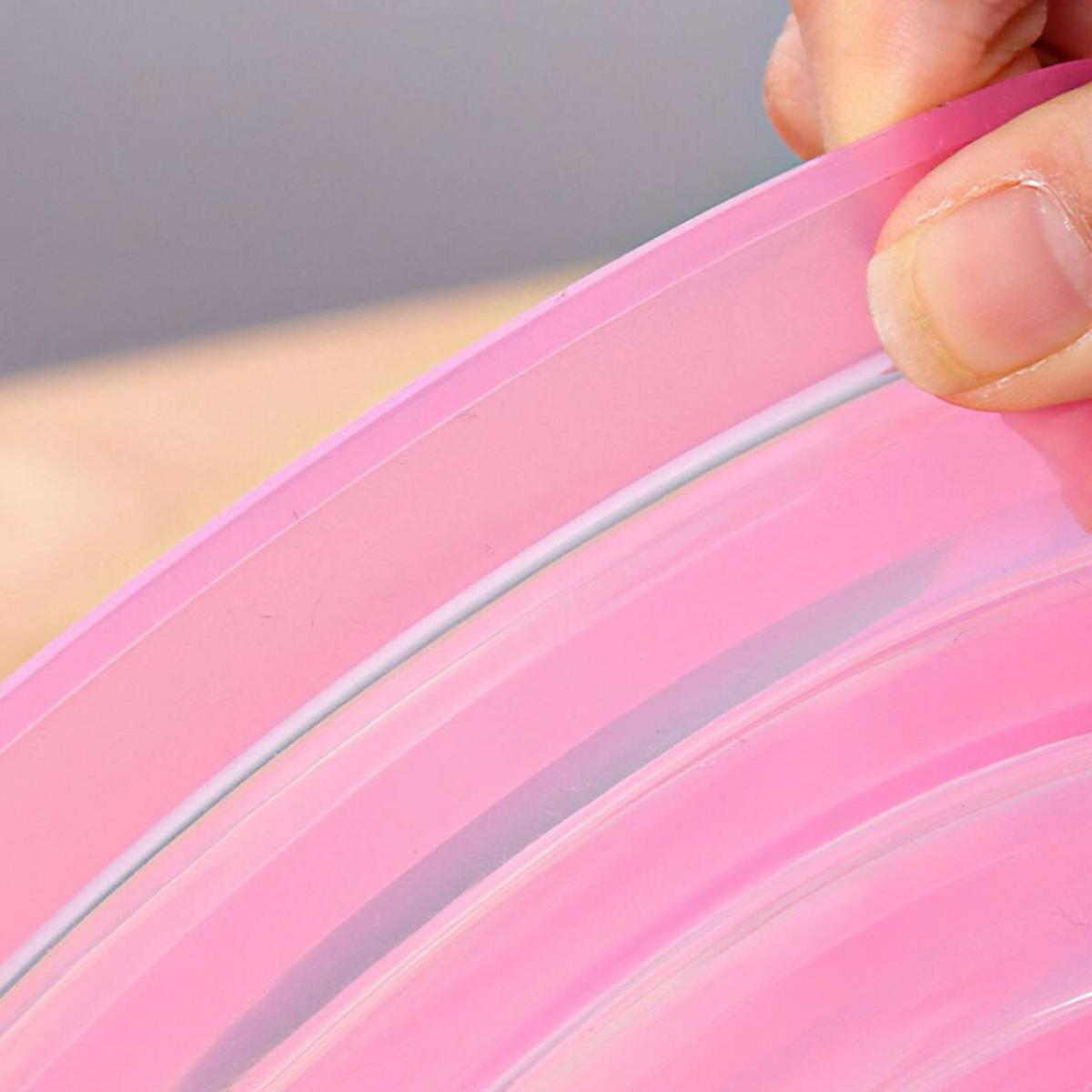 Eine Hand hält den Rand einer rosa Plastiktüte. Die Tasche hat einen Reißverschluss. Der Hintergrund ist hellgrau und hautfarben.