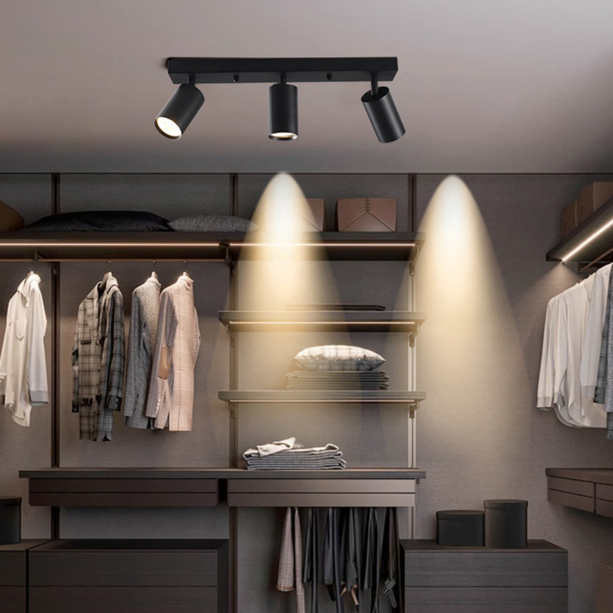 Schwarze Strahler beleuchten einen Schrank mit Kleidung, Regalen und Schubladen. Neutrale Töne dominieren. Garderobe ist gut organisiert.