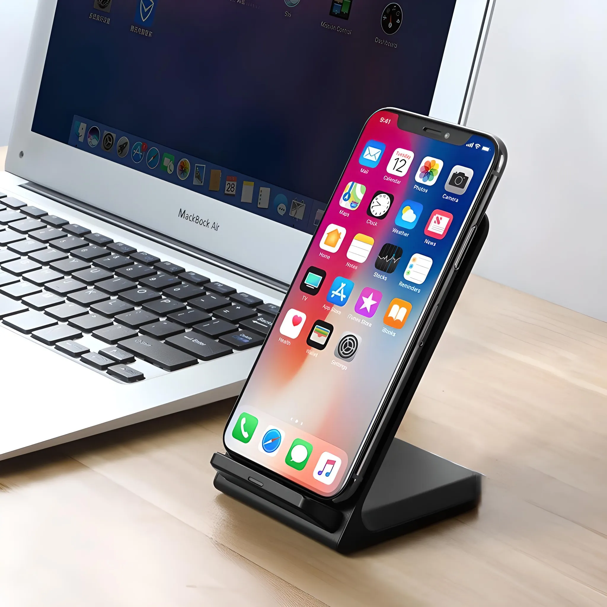 Ein iPhone auf einem Ständer steht vor einem Macbook. Das iPhone zeigt Apps an. Das Macbook ist auf einem Holztisch geöffnet.