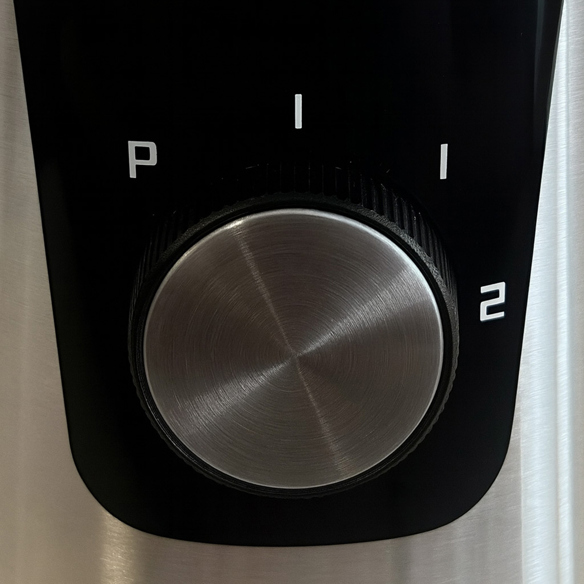 Primer plano de un panel de control negro con una perilla plateada. Letras y números blancos indican ajustes: P, I, 1 y 2.