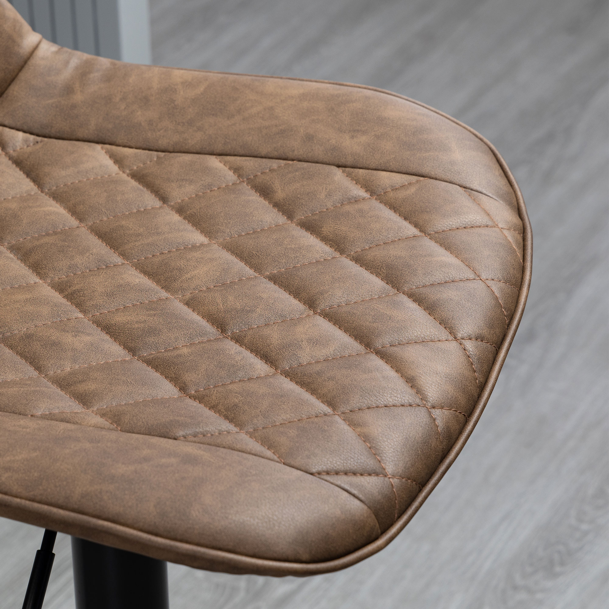 Primer plano de un asiento de silla de cuero marrón con costuras de diamante. El fondo es un piso gris y parte de una pared.
