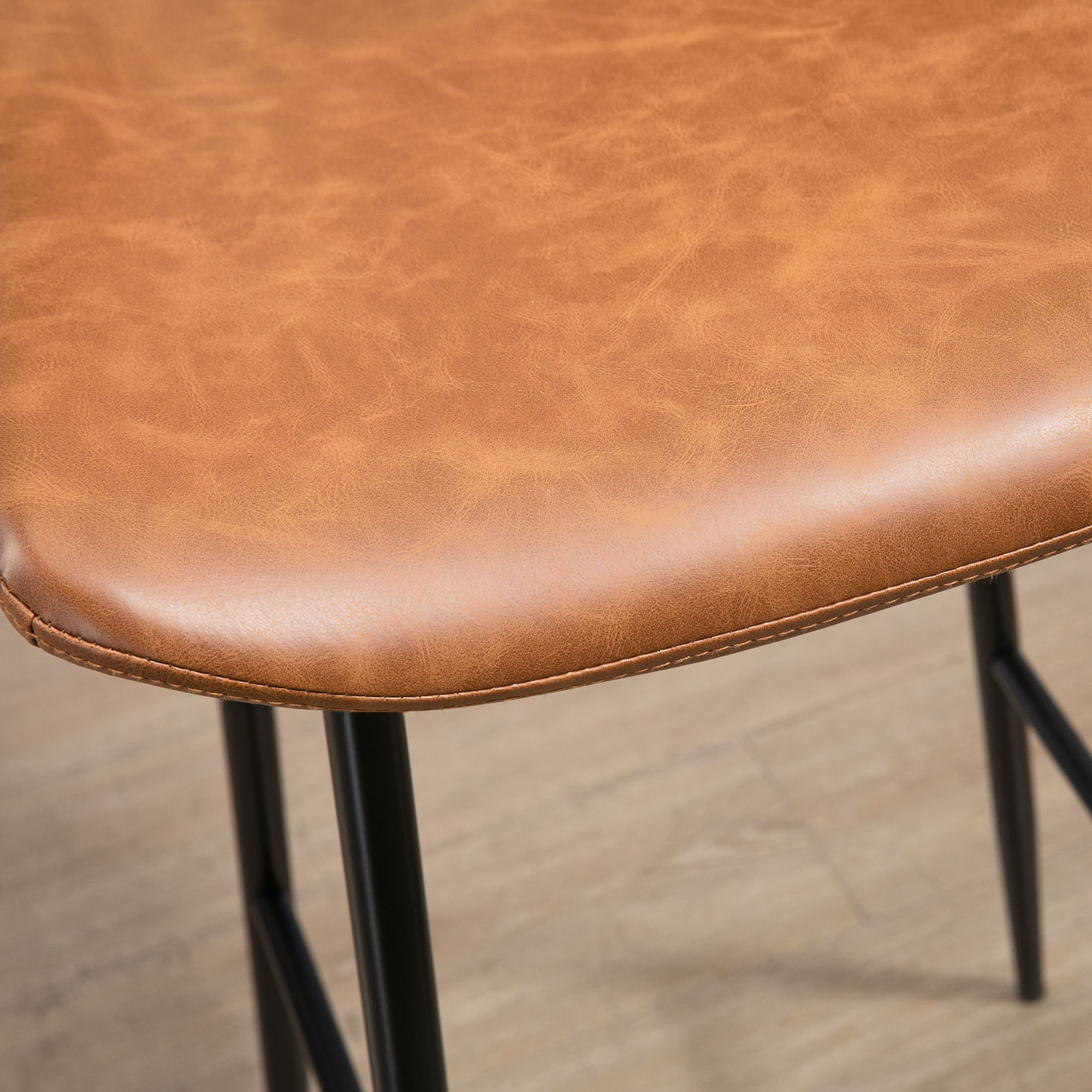 Primer plano de un asiento de silla de cuero marrón con patas de metal negro sobre piso de madera.