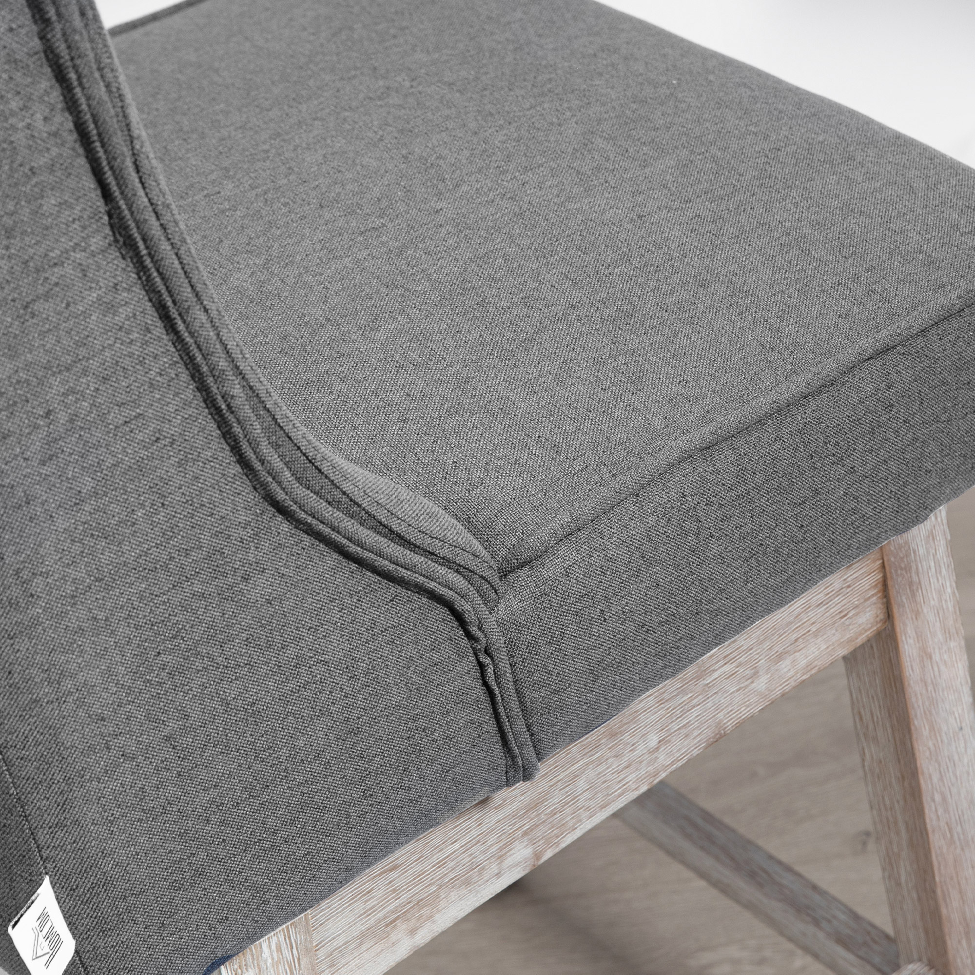 Primer plano de una silla tapizada gris. El marco de madera es visible. El asiento tiene una textura detallada.