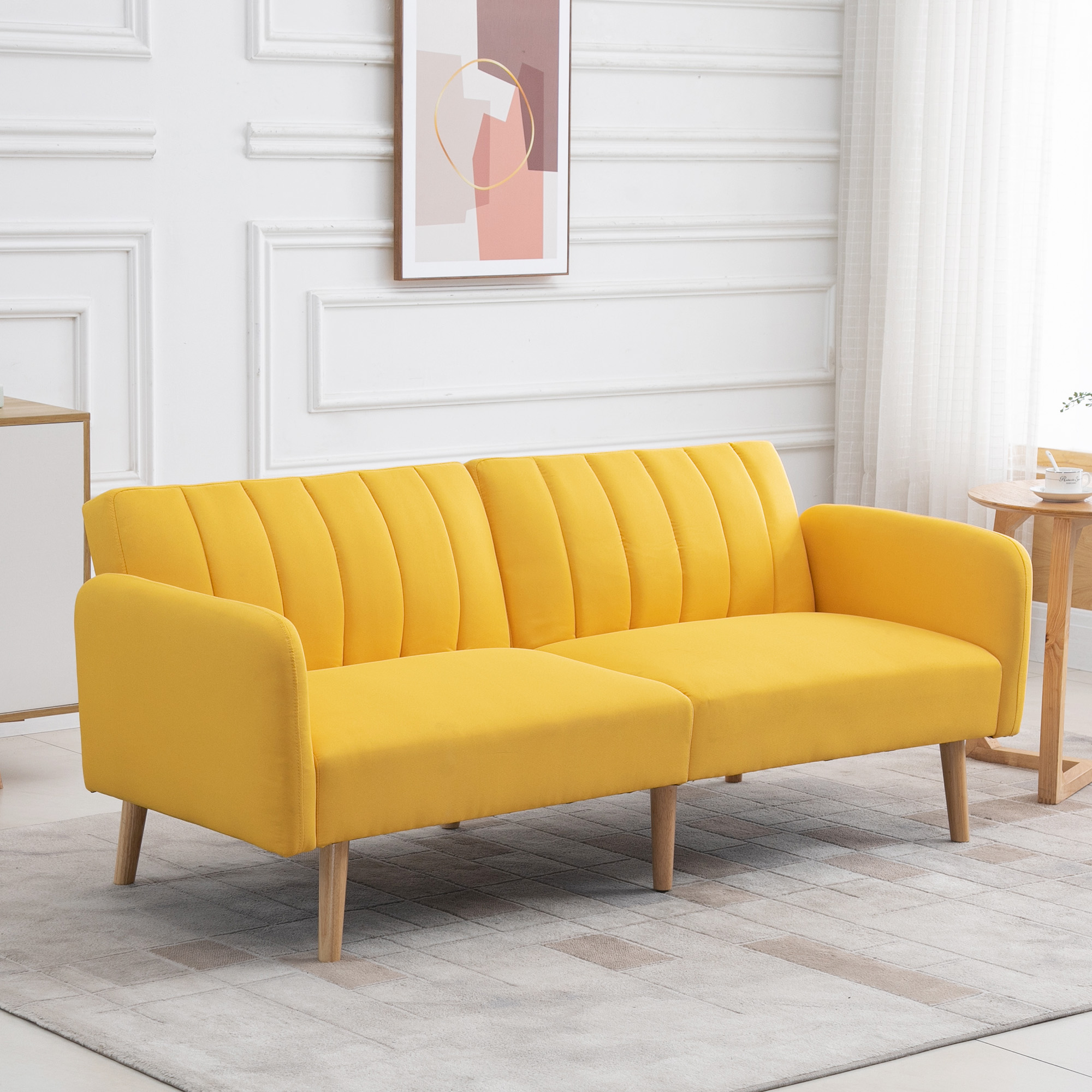 Un sofá amarillo en una habitación. Hay una pintura en la pared. Se ven un armario blanco y una mesa de madera pequeña.