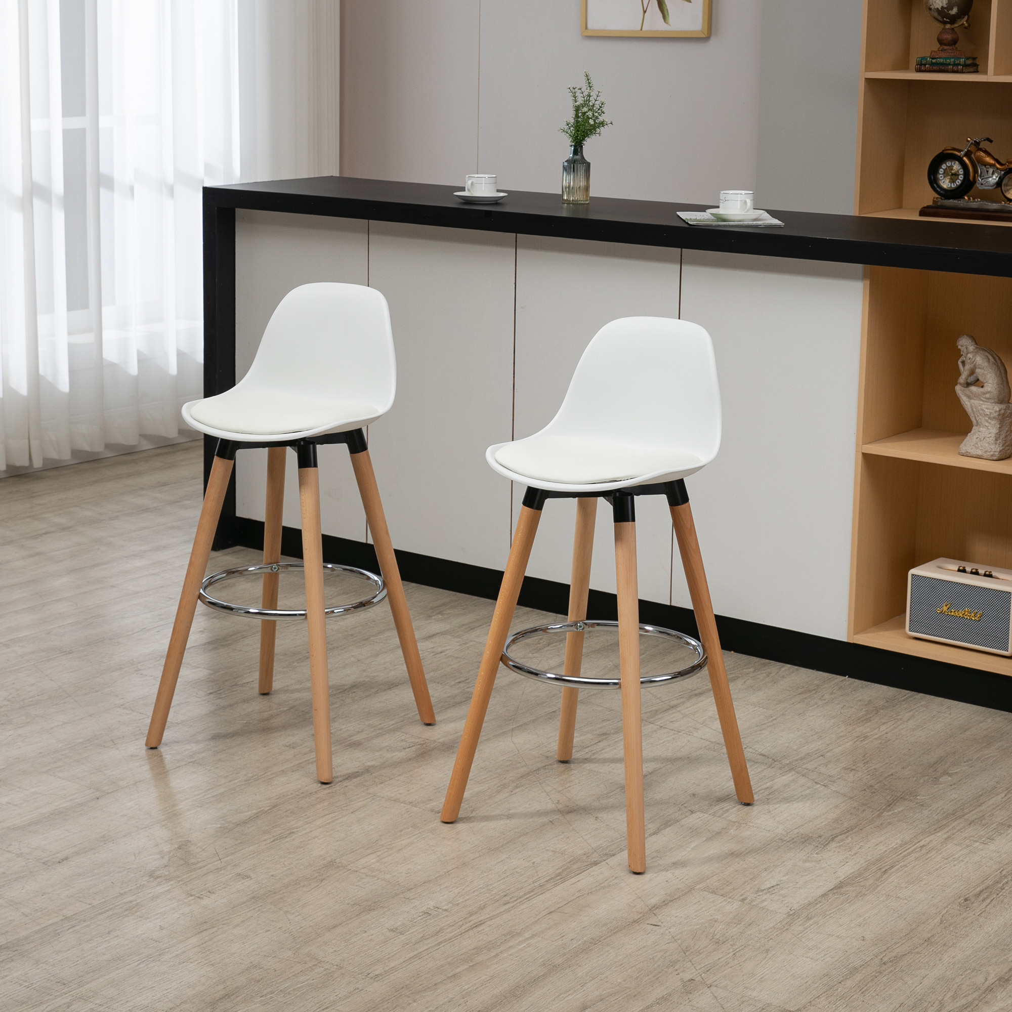 Dos taburetes blancos con patas de madera frente a una barra negra. Un jarrón y tazas están sobre la barra.
