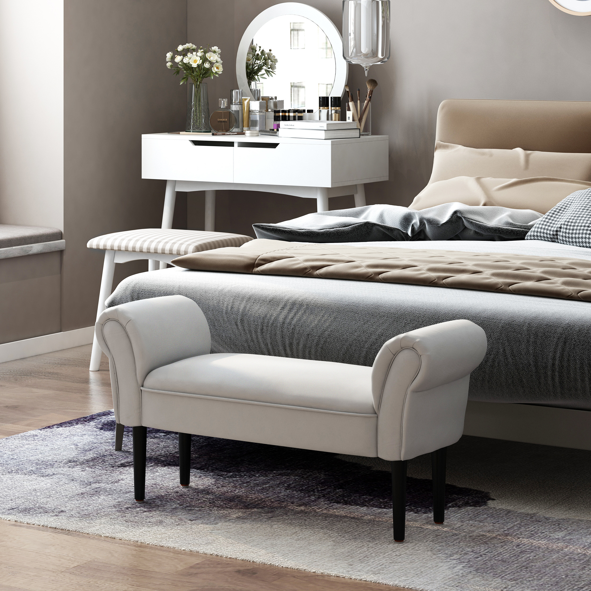 Dormitorio con cama, banco blanco, tocador con espejo y flores. Colores neutros y luz natural.
