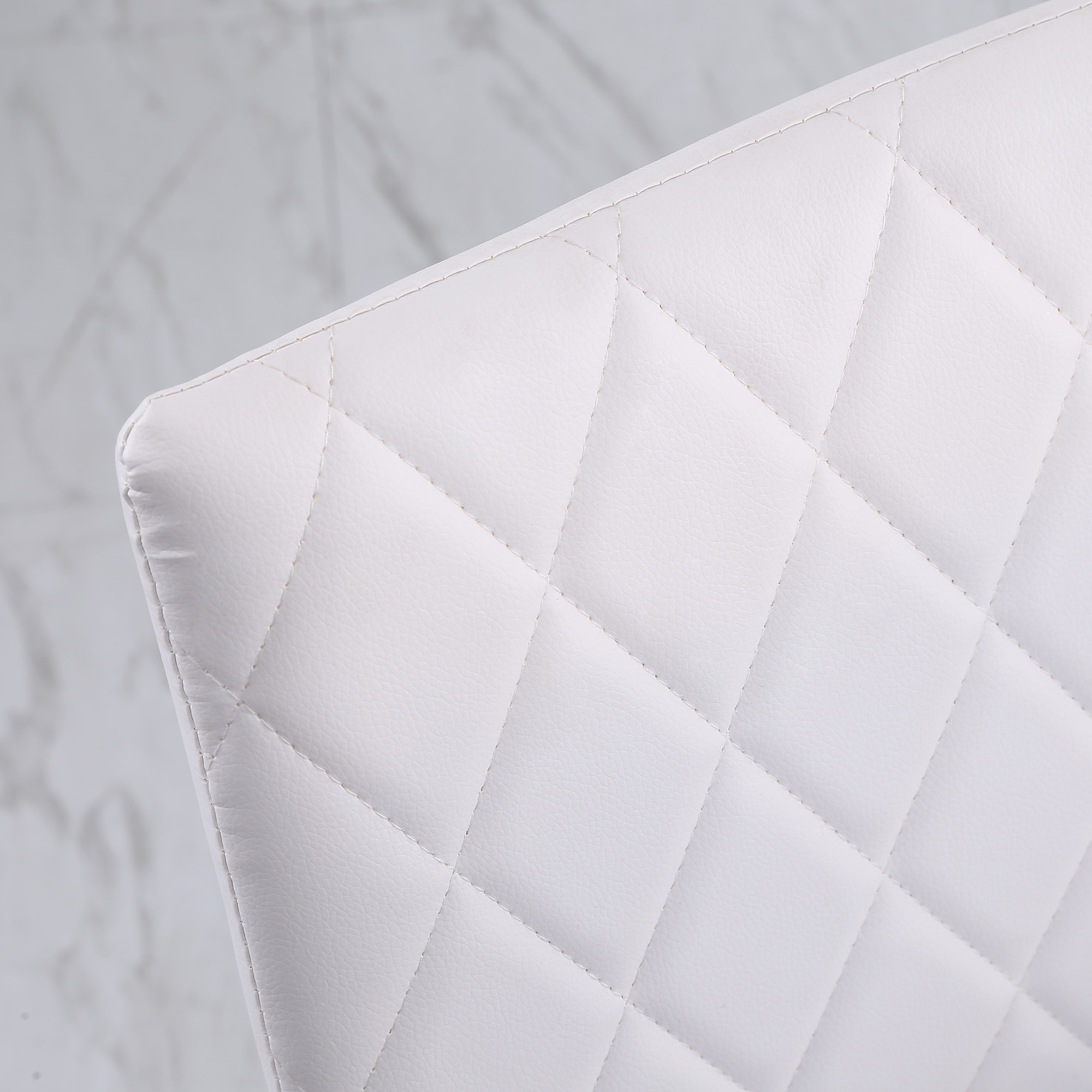 Primer plano del respaldo de una silla blanca con costuras de diamante. El fondo es una superficie borrosa de mármol blanco.