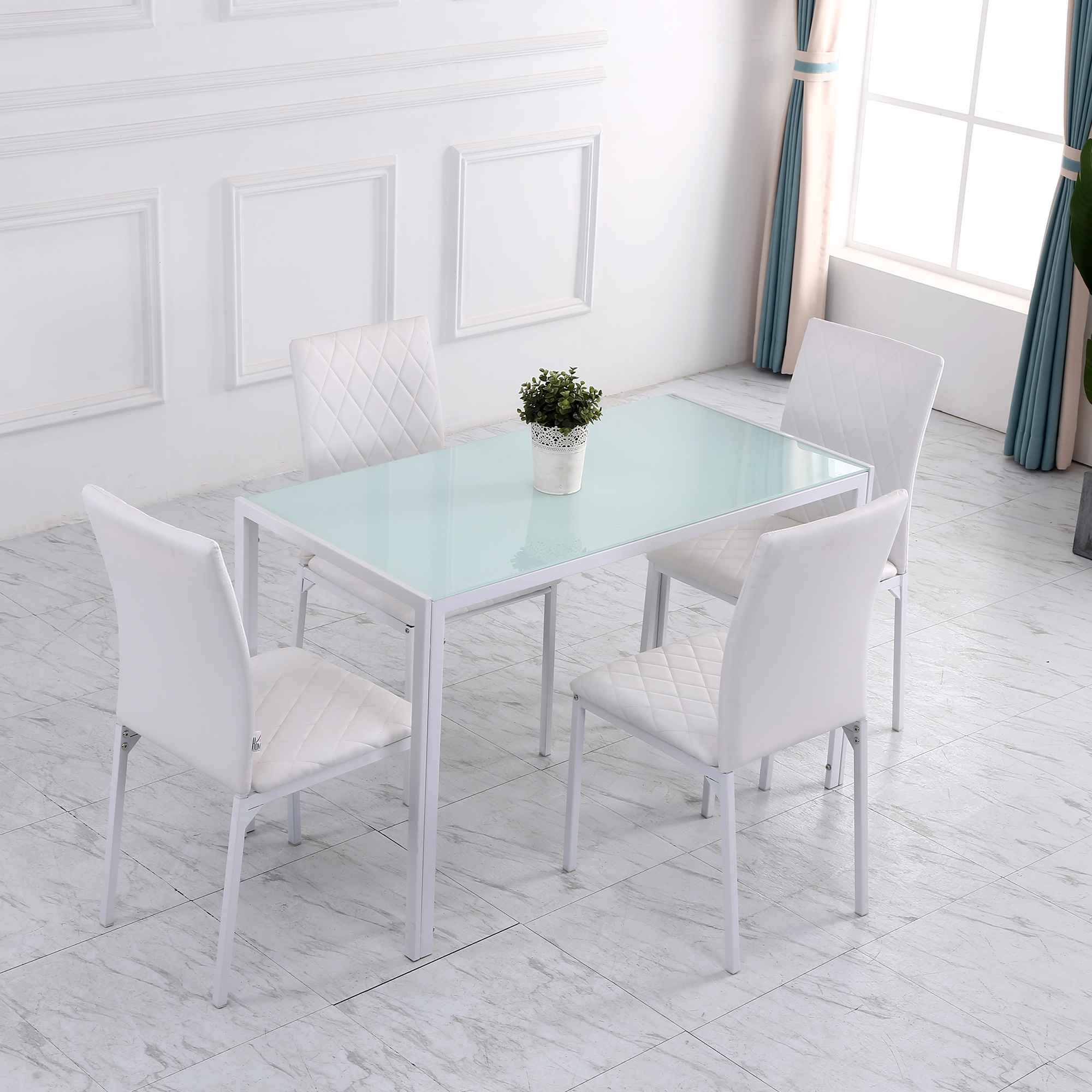 Un juego de comedor blanco con una mesa con tapa de vidrio y cuatro sillas blancas. Una pequeña planta en el centro de la mesa.