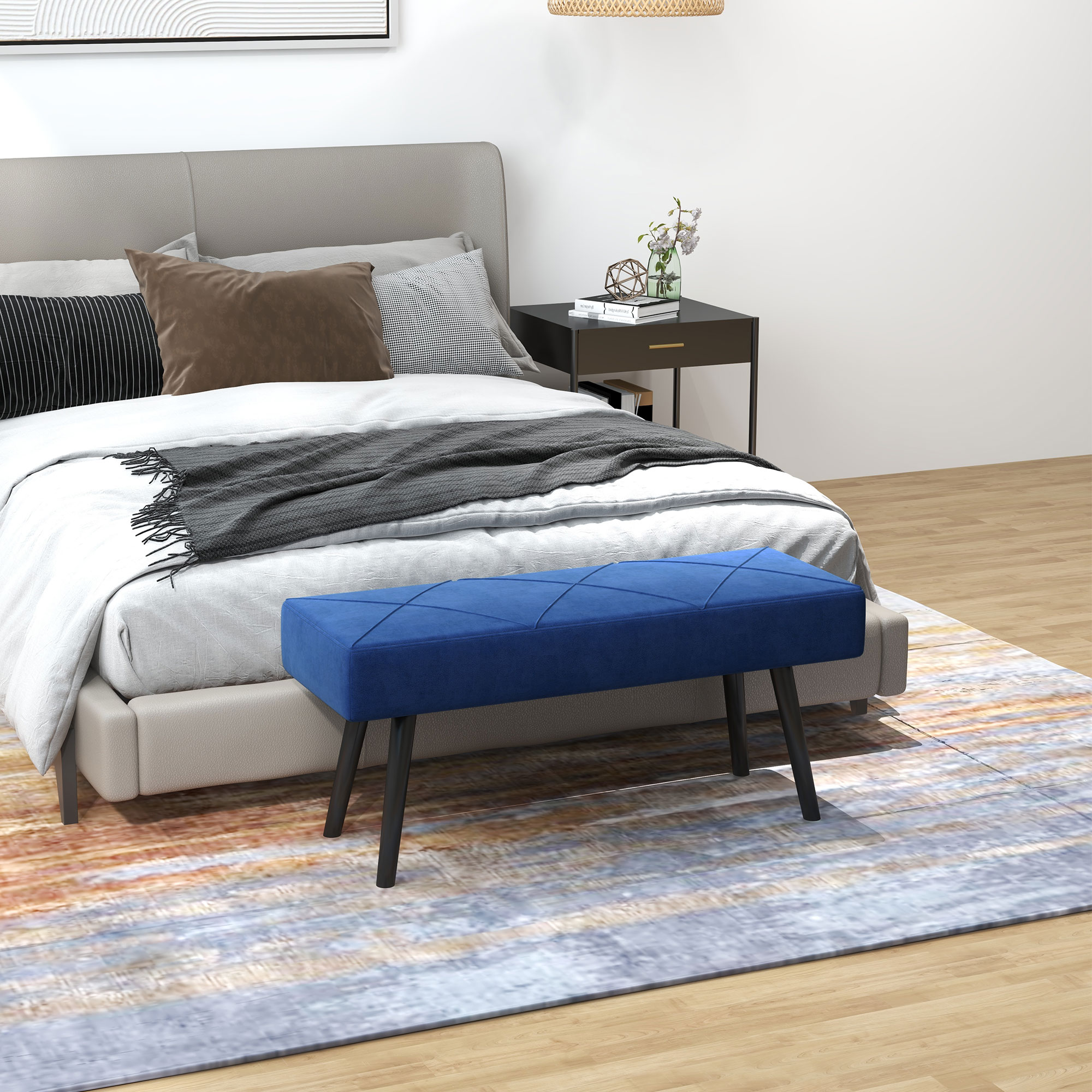 Dormitorio con cama, almohadas, banco azul, alfombra y mesita de noche.