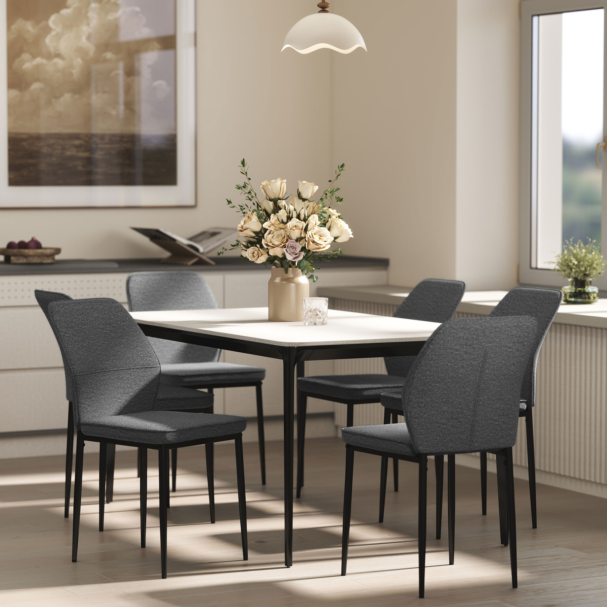 Un comedor con mesa, sillas, flores y ventana. Luz de una lámpara colgante. Una pintura en la pared.