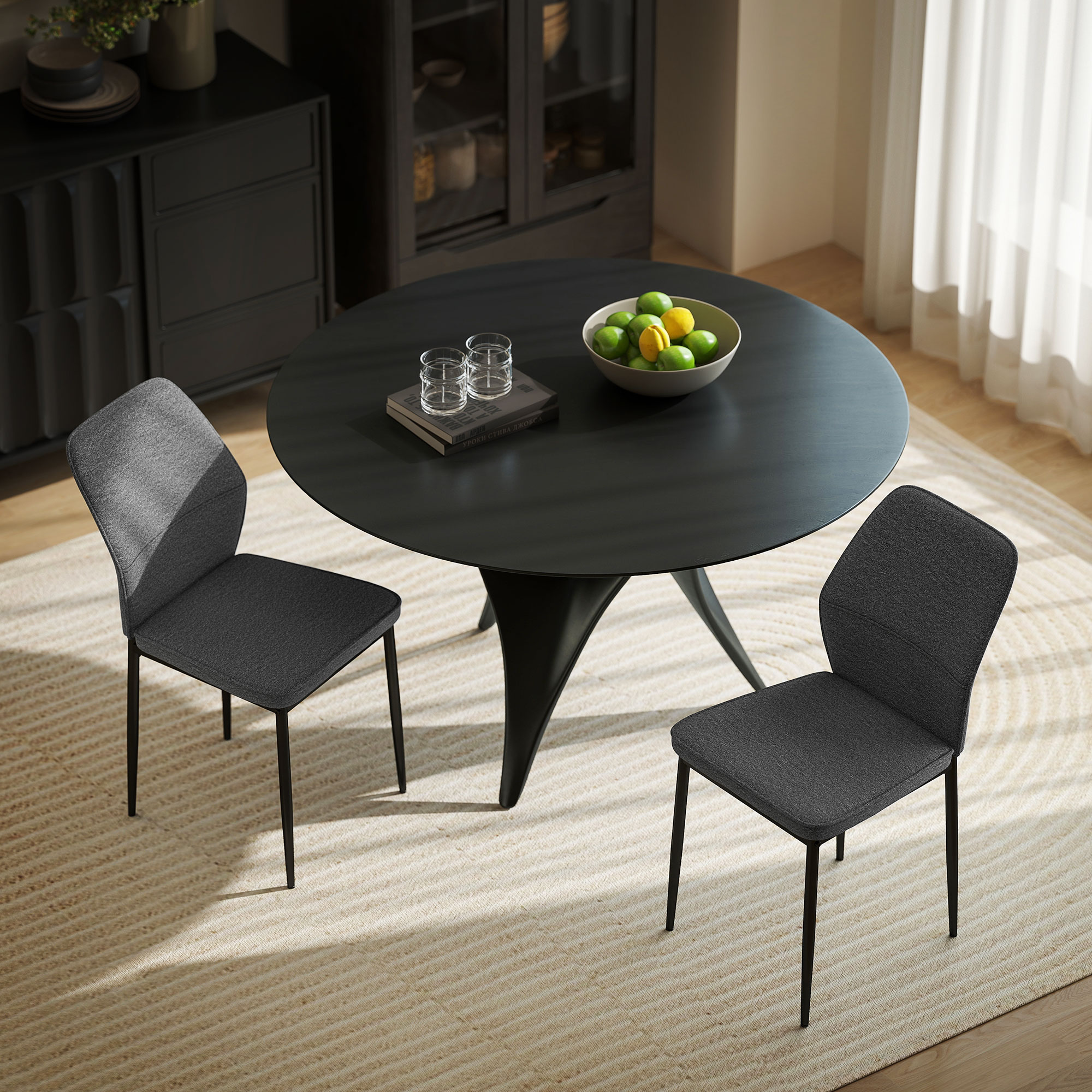 Una mesa redonda negra con dos sillas grises, un frutero y dos vasos. La habitación tiene una alfombra y un armario.