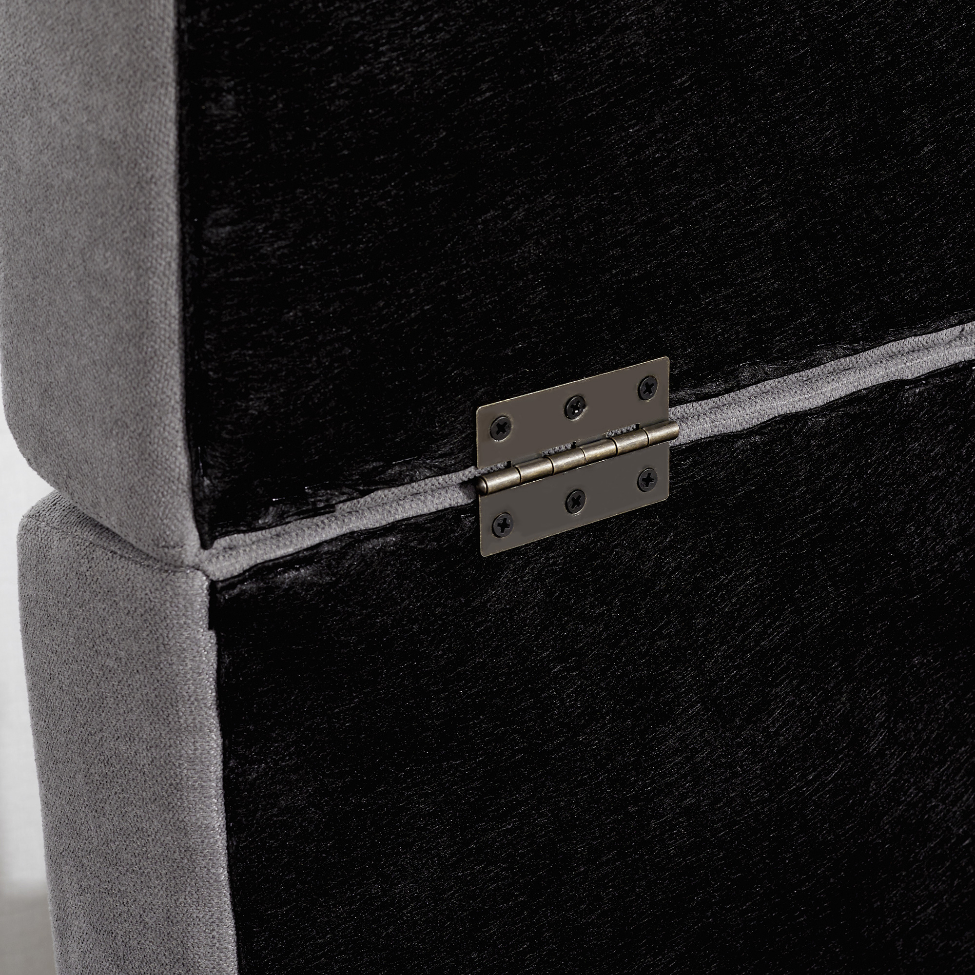 Primer plano de una esquina de mueble tapizado gris. Un panel negro está unido con una bisagra.