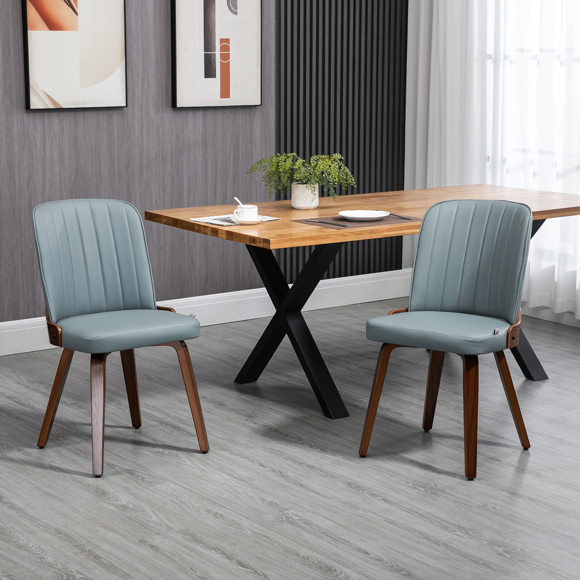 Dos sillas azules con patas de madera frente a una mesa de madera. Una planta en la mesa, arte en la pared.