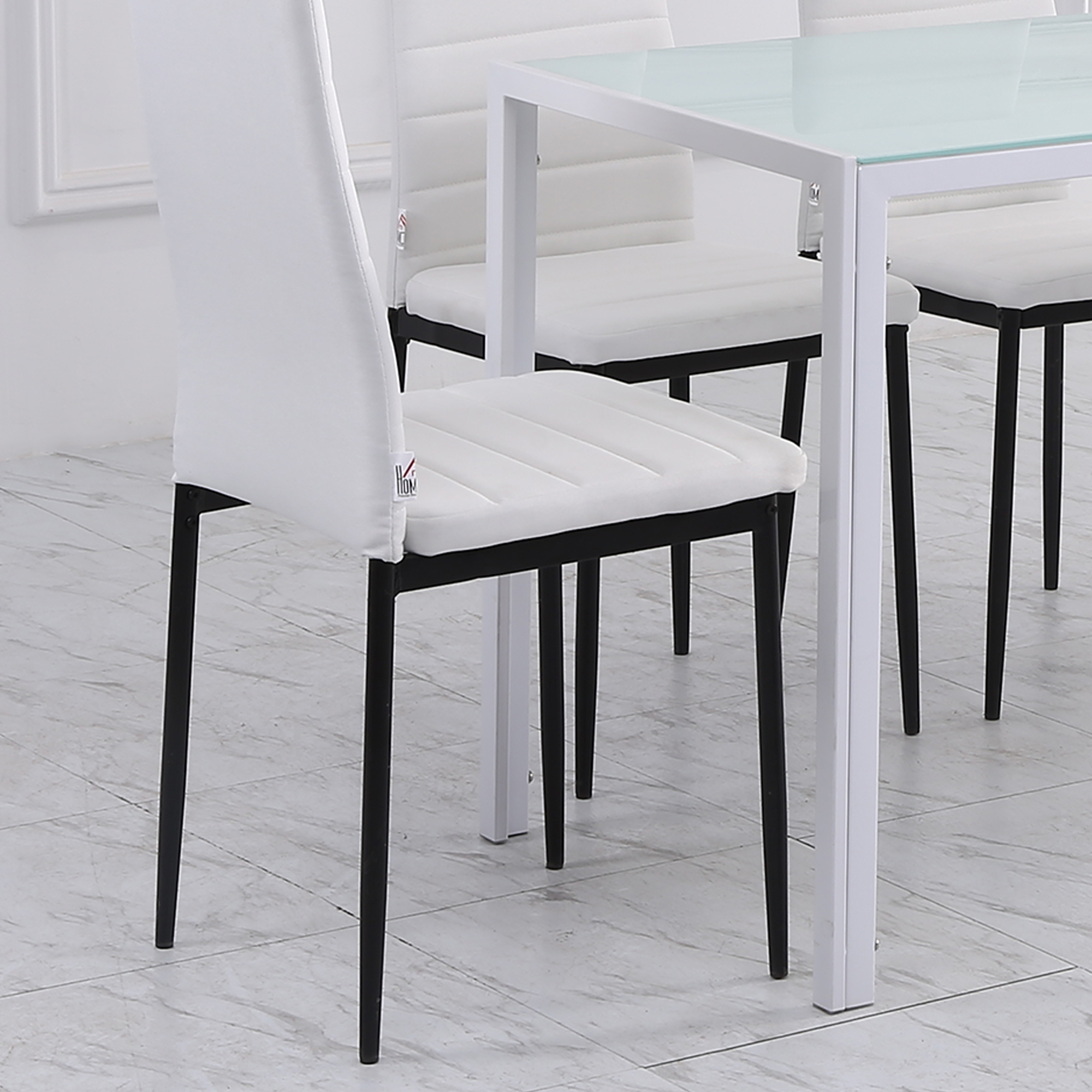 Sillas de comedor blancas con patas negras debajo de una mesa de cristal con patas de metal blanco. El suelo está embaldosado.