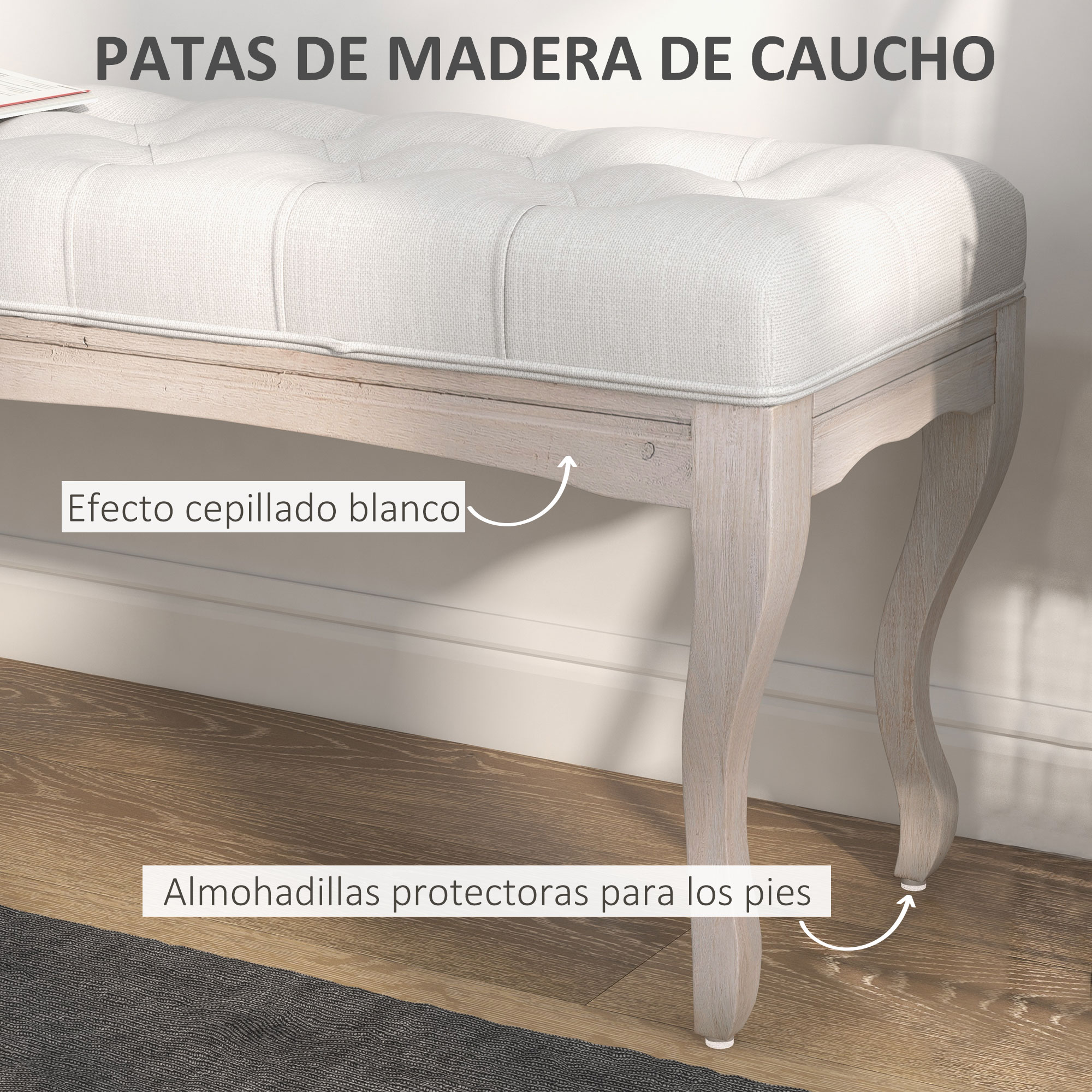 Un banco acolchado blanco con patas de madera. Las patas tienen un efecto blanco cepillado. El suelo es de madera, y debajo hay una alfombra.