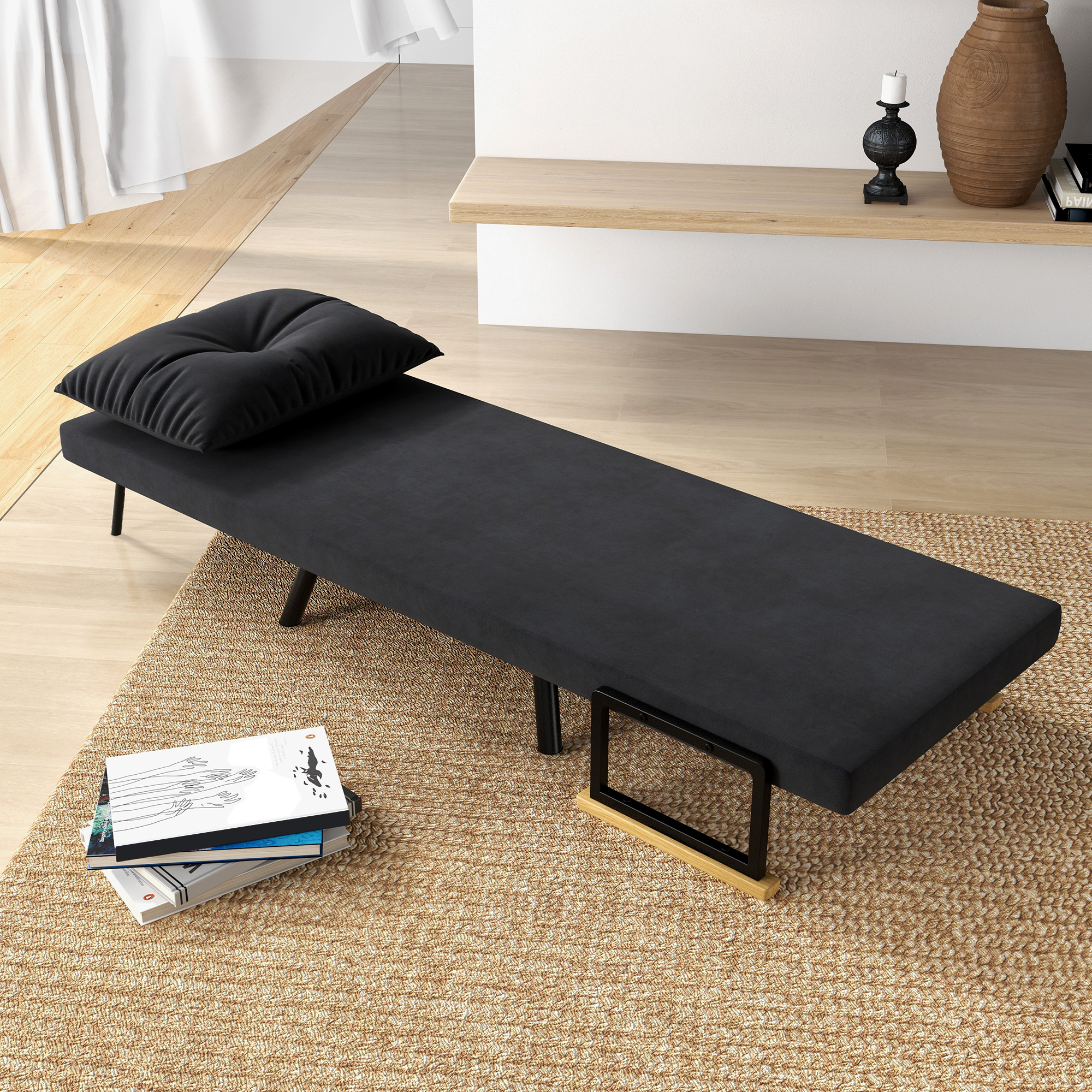 Un sofá cama negro con una almohada está sobre una alfombra tejida, hay libros cerca. Una vela y un jarrón están en un estante.