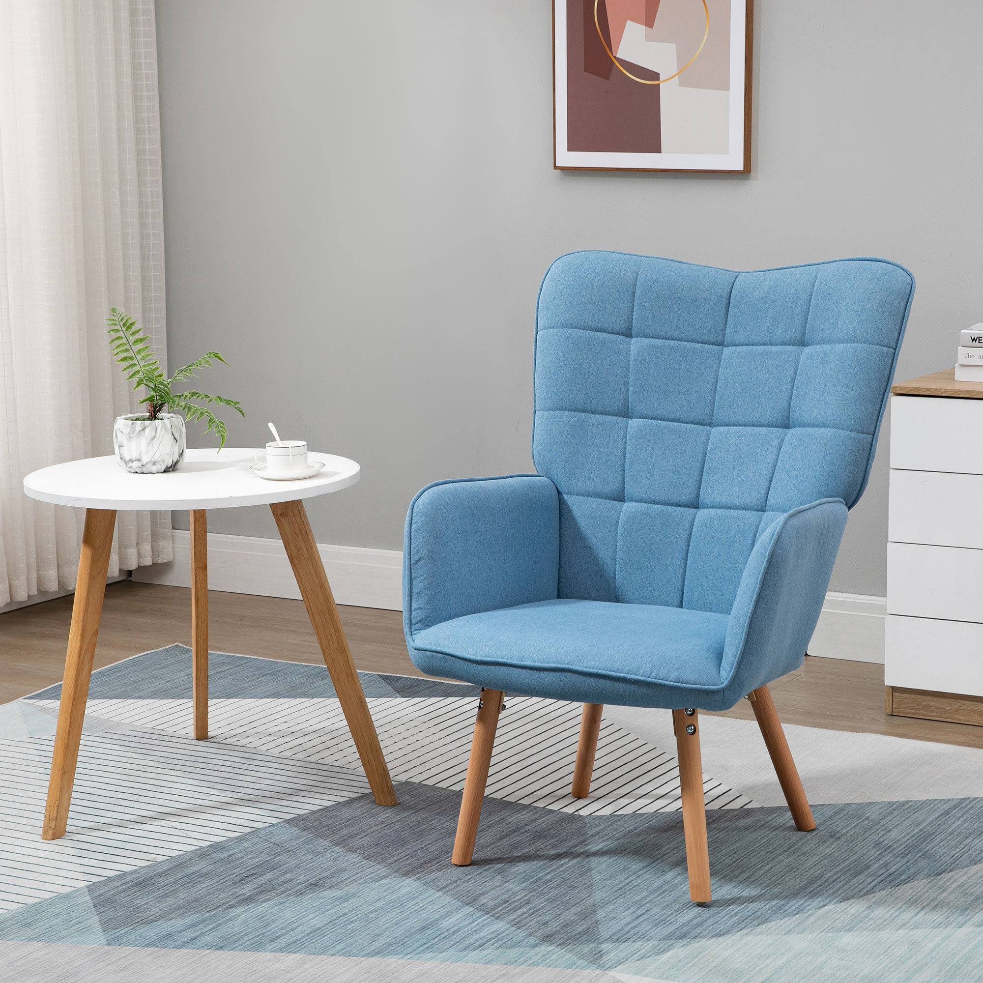 Un sillón azul junto a una mesa blanca con una planta y una taza. Un cuadro cuelga en la pared.