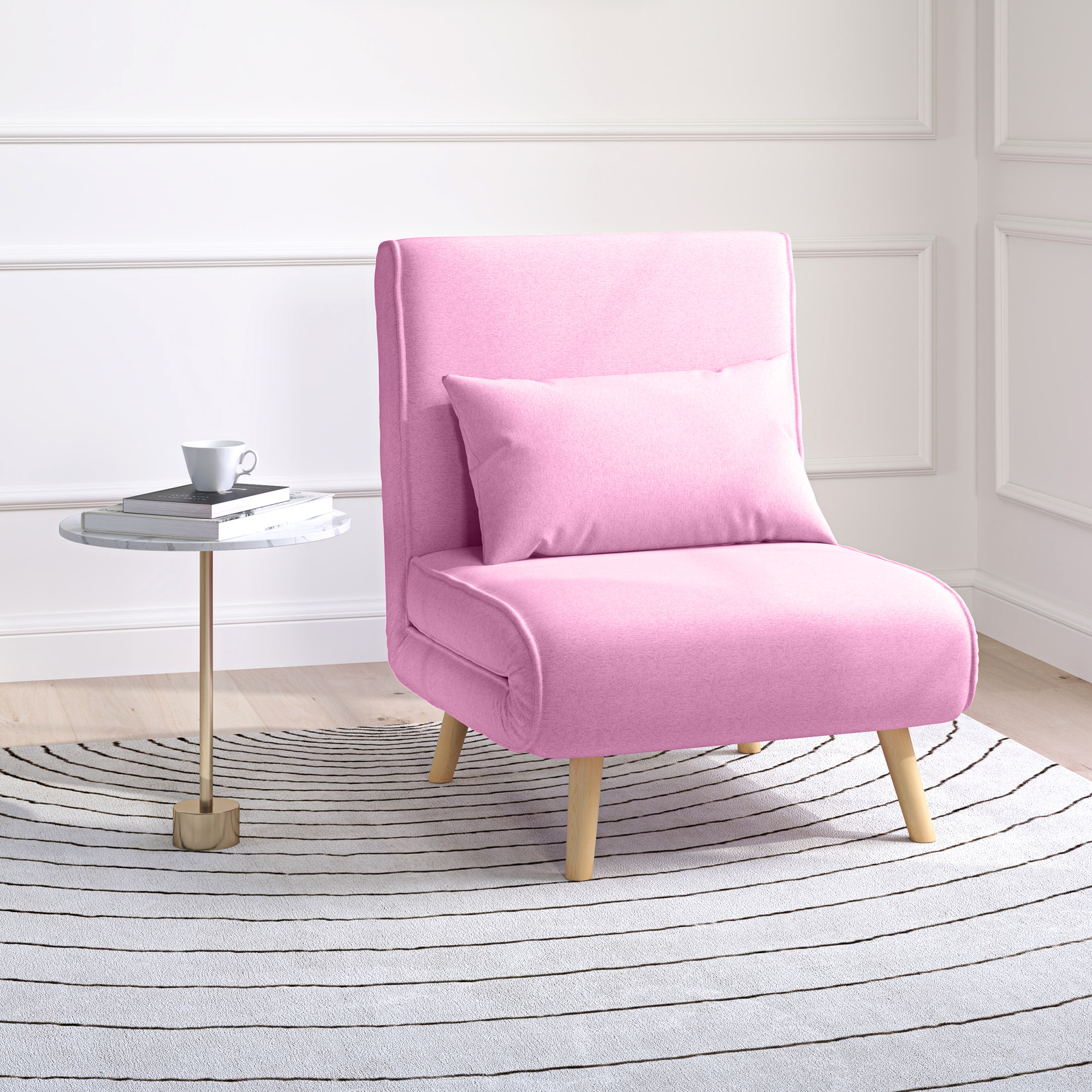 Silla rosa con almohada sobre una alfombra a rayas cerca de una mesa pequeña con libros y una taza.
