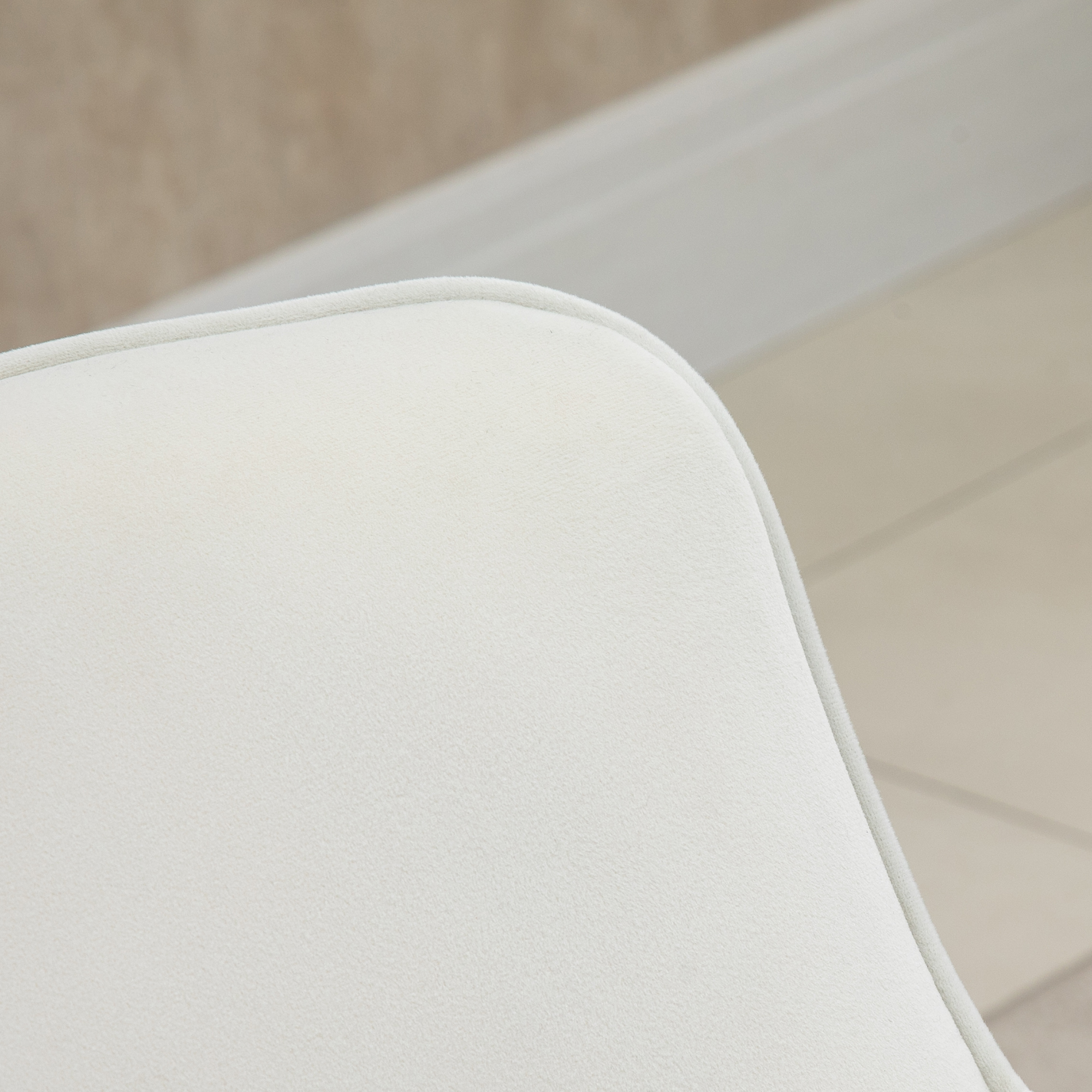 Primer plano de una superficie blanca acolchada con borde redondeado. Fondo: pared beige y paneles blancos.