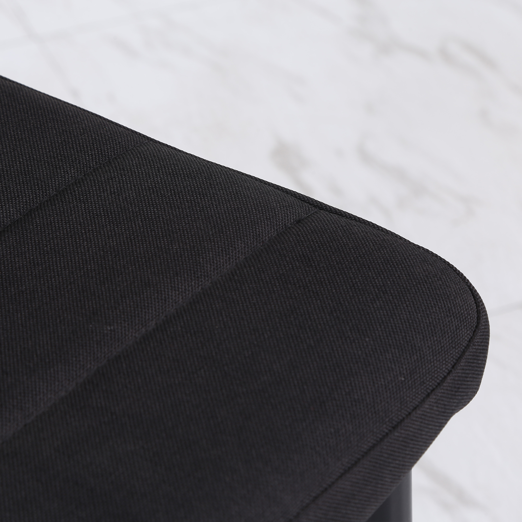 Primer plano de un asiento de silla negro y acolchado con costuras verticales. El fondo es una superficie borrosa y clara.