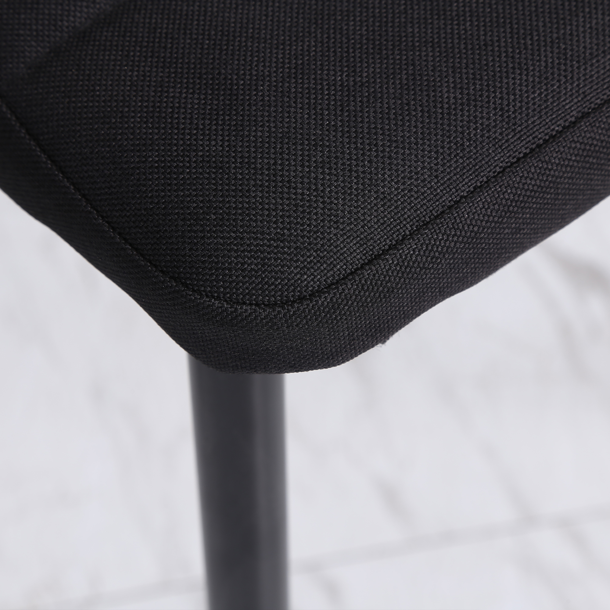 Primer plano de un cojín de silla negro. La tela es texturizada. Se ve una pata negra. El fondo es blanco borroso.