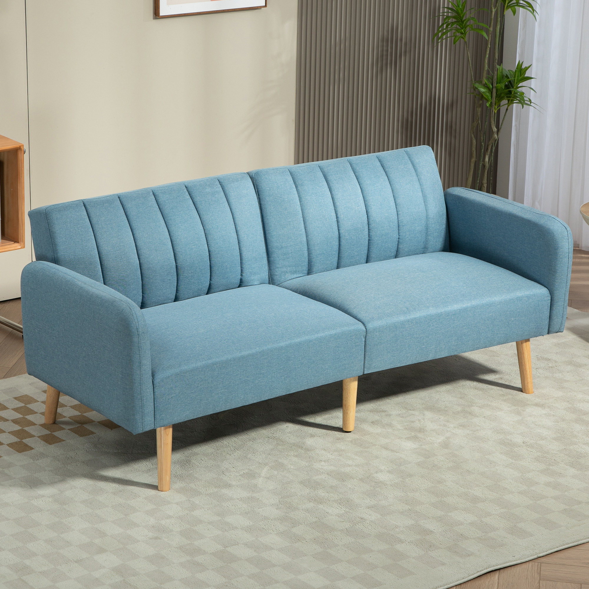 Un sofá azul con patas de madera sobre una alfombra estampada. El fondo incluye una planta y una pared.