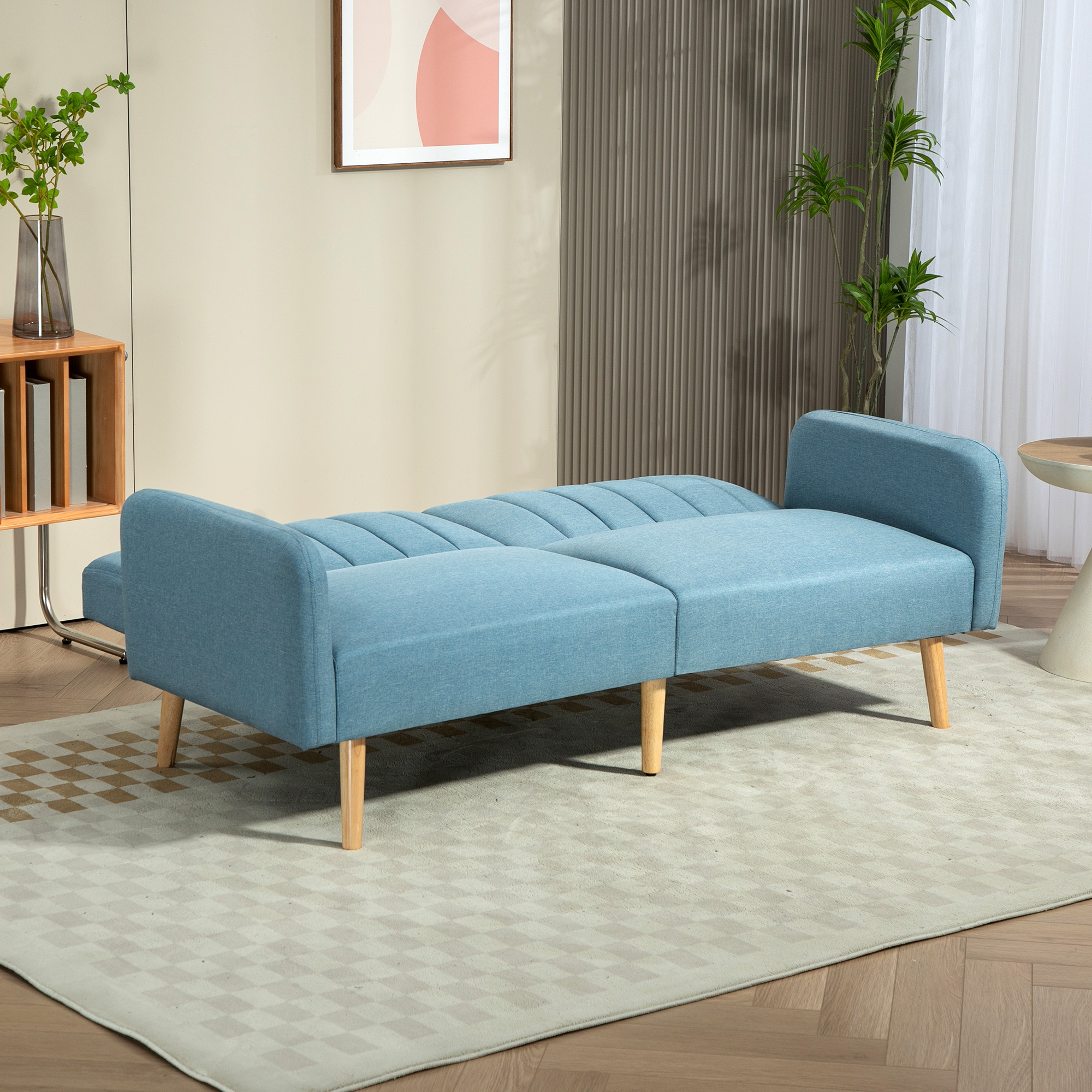 Un sofá azul con patas de madera está sobre una alfombra estampada. Plantas, una pintura y una mesa en el fondo.
