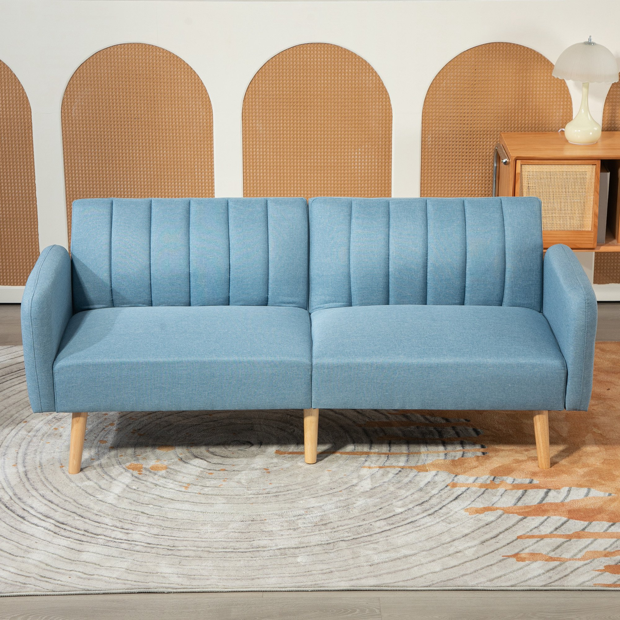 Un sofá azul con patas de madera está sobre una alfombra estampada. El fondo tiene arcos y un mueble de madera con lámpara.