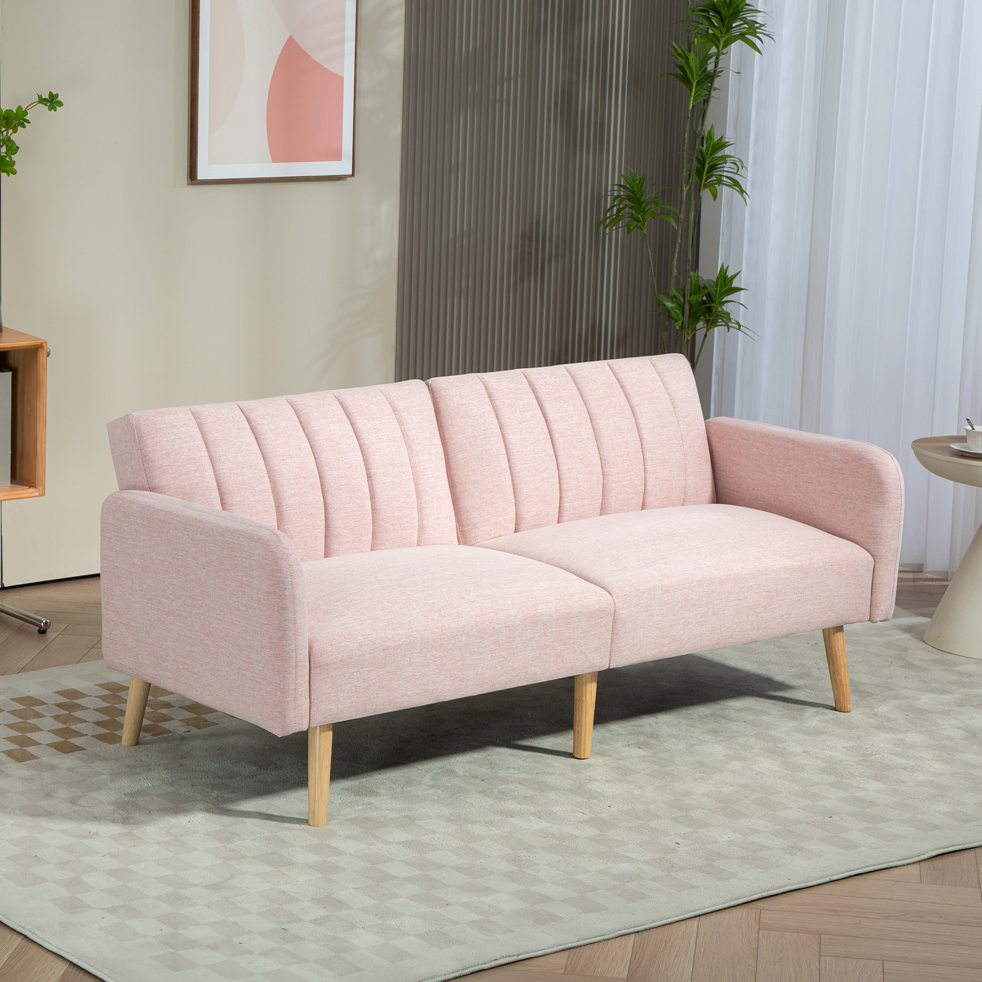 Un sofá rosa con patas de madera sobre una alfombra estampada. Una imagen y plantas al fondo.