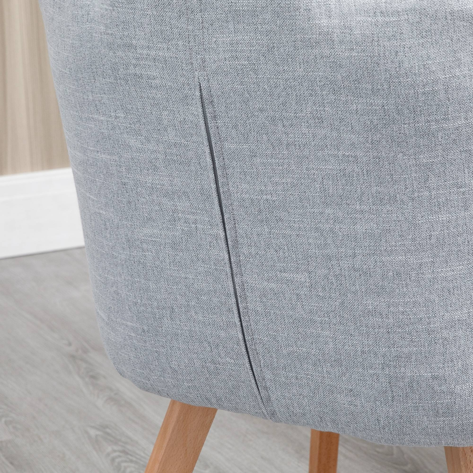 Primer plano de una silla de tela gris. Las patas de madera son visibles en la parte inferior. El fondo tiene una pared de madera clara.