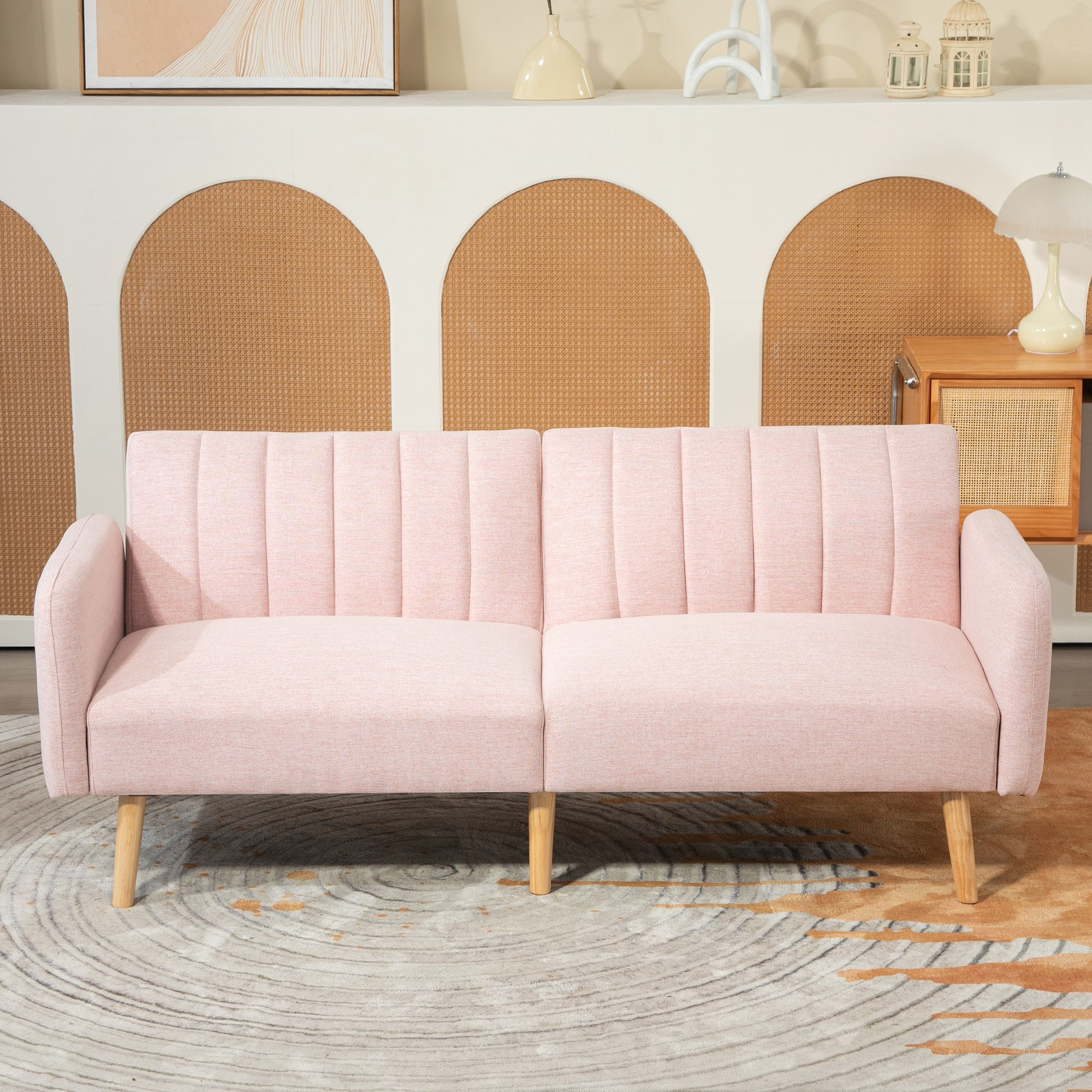 Un sofá rosa frente a una pared con arcos. Una mesa de madera con una lámpara a la derecha.