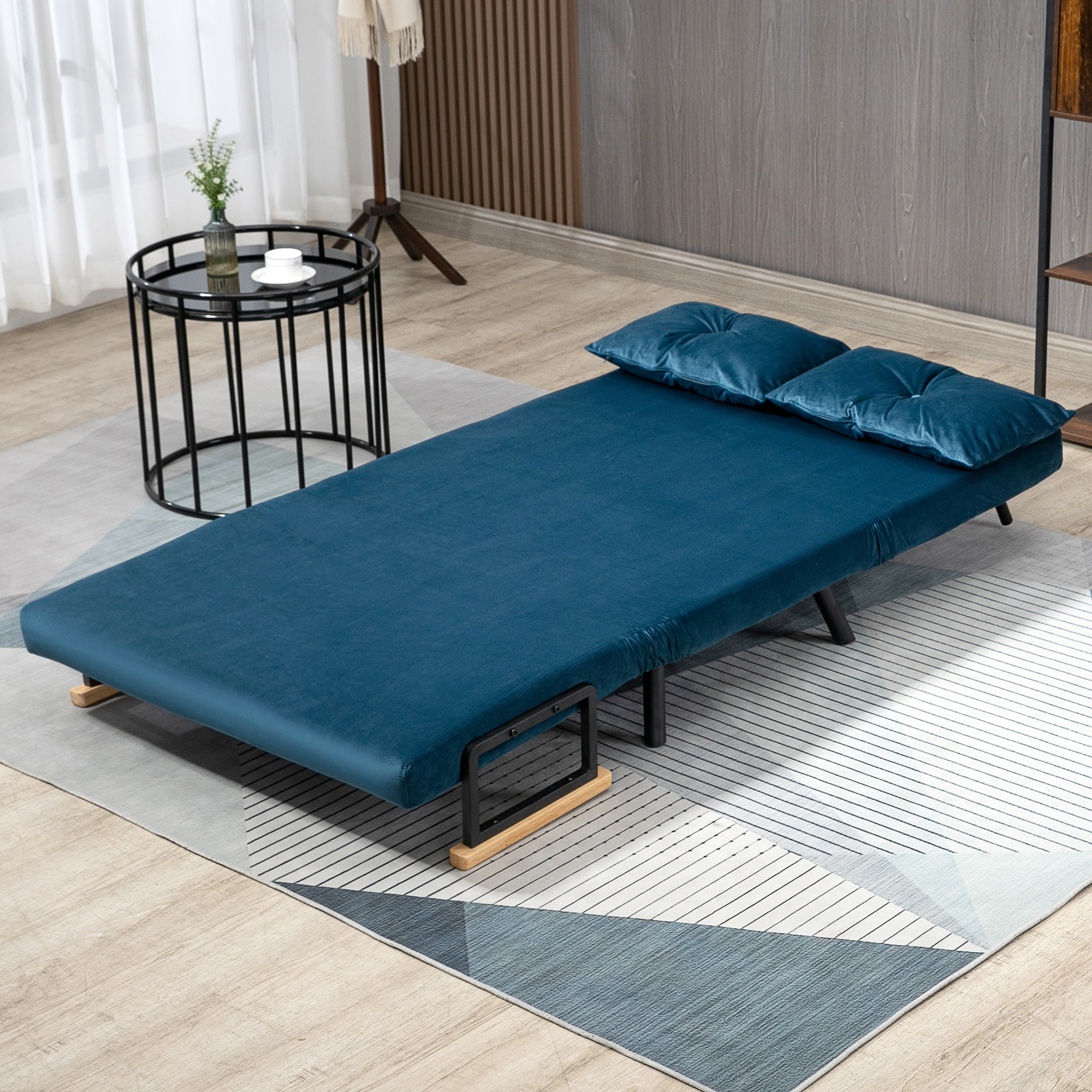 Un sofá cama azul con almohadas sobre una alfombra estampada. Una mesita con una taza a la izquierda.