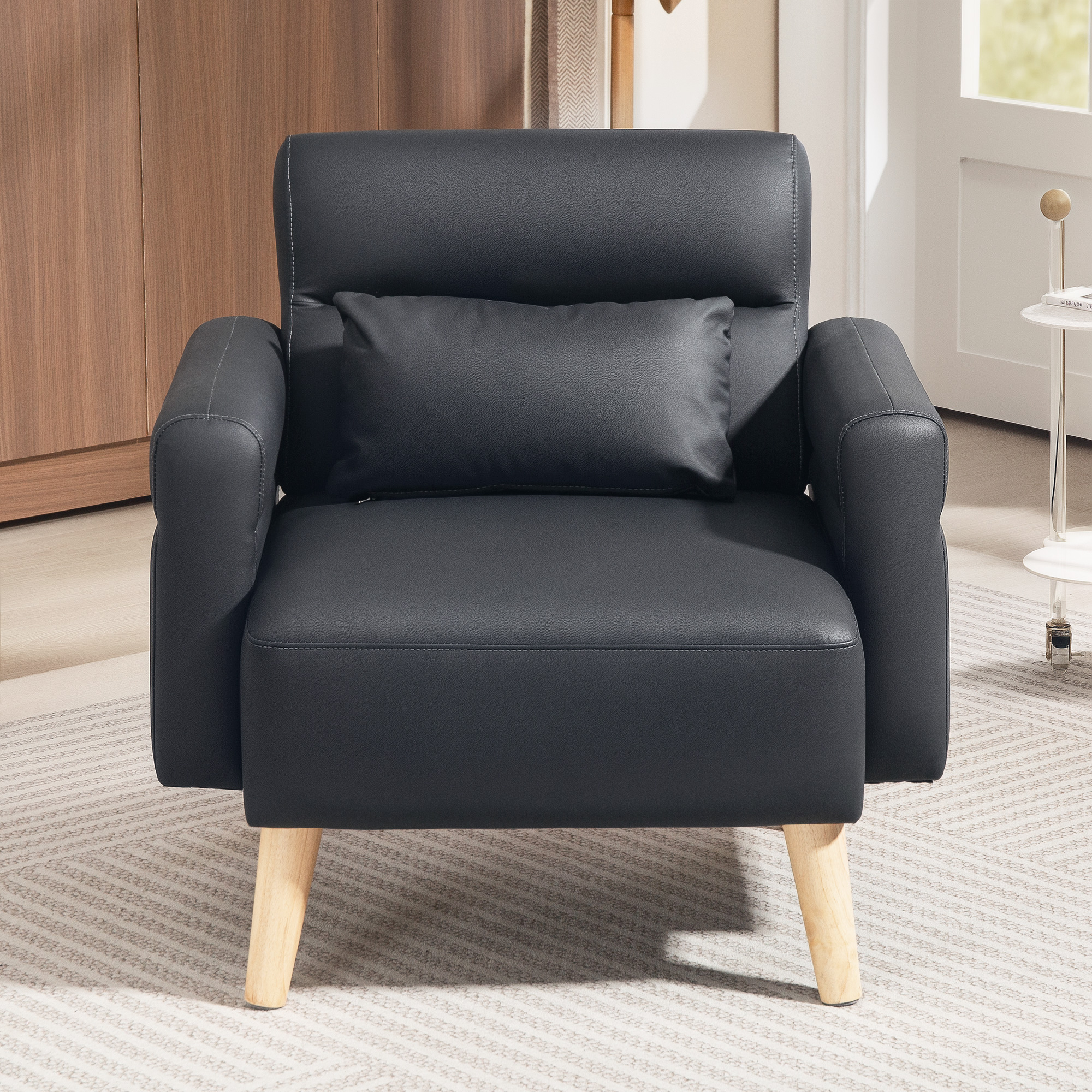 Sillón negro con almohada sobre una alfombra estampada. Patas de madera y mesita blanca al fondo.