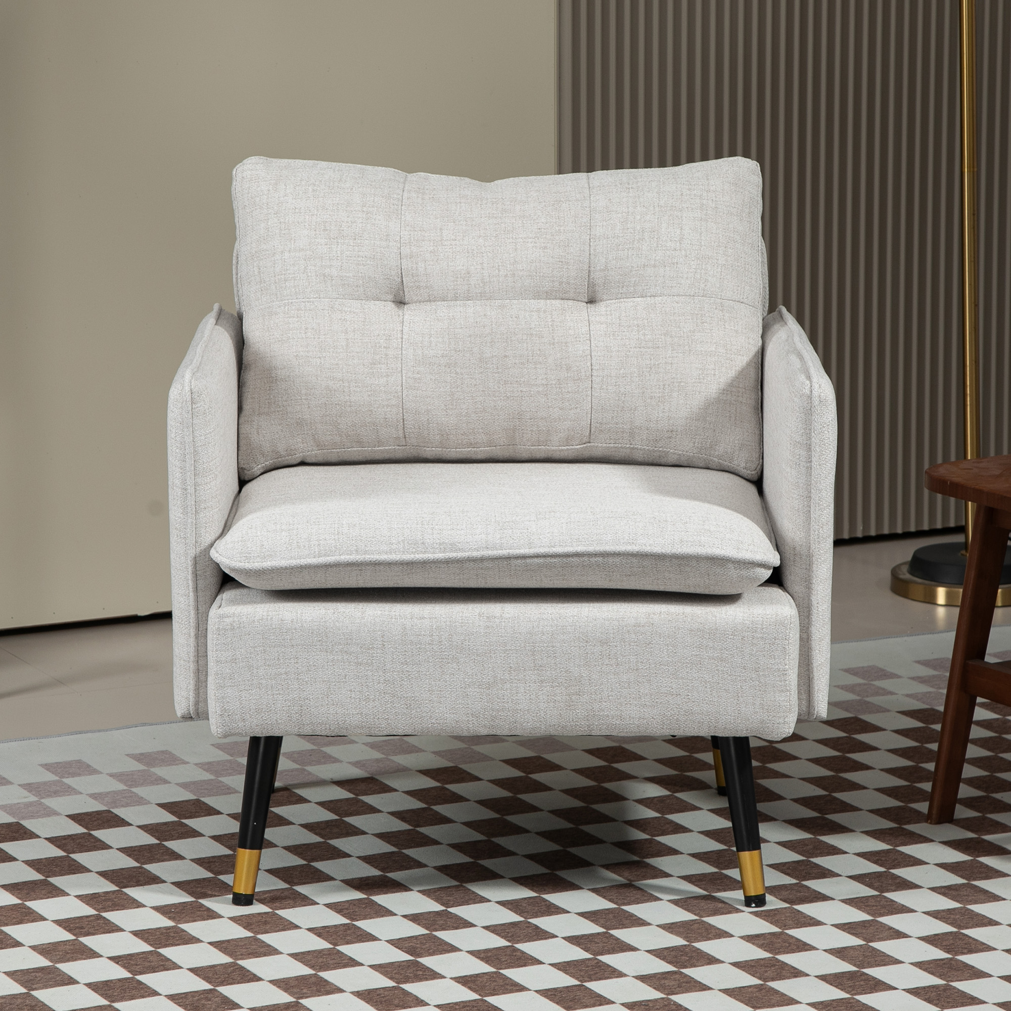 Un sillón gris claro con patas negras y puntas doradas, sobre una alfombra a cuadros.