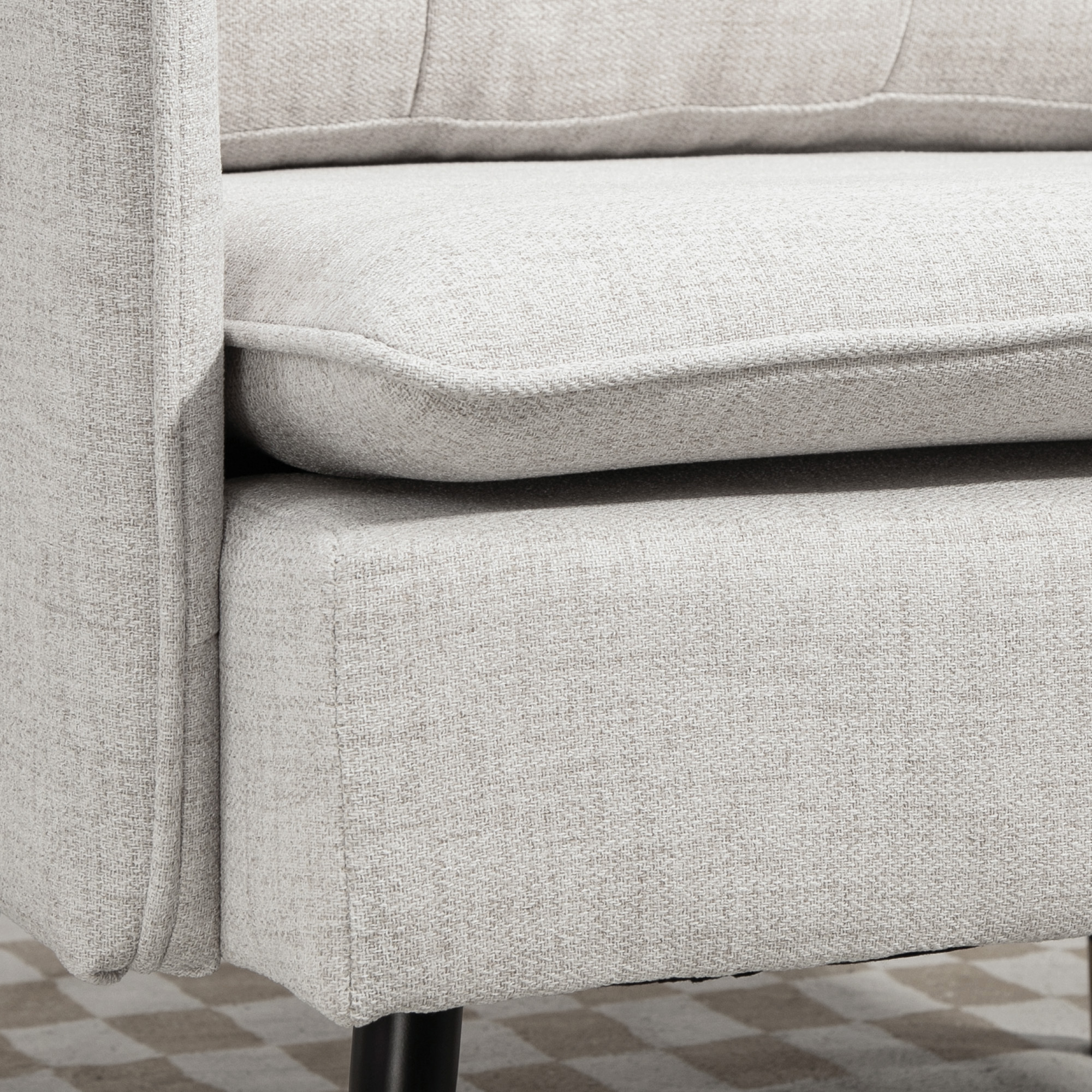Primer plano de un sillón de tela gris claro. Se ven el reposabrazos, el cojín y el asiento con un suelo a cuadros de fondo.