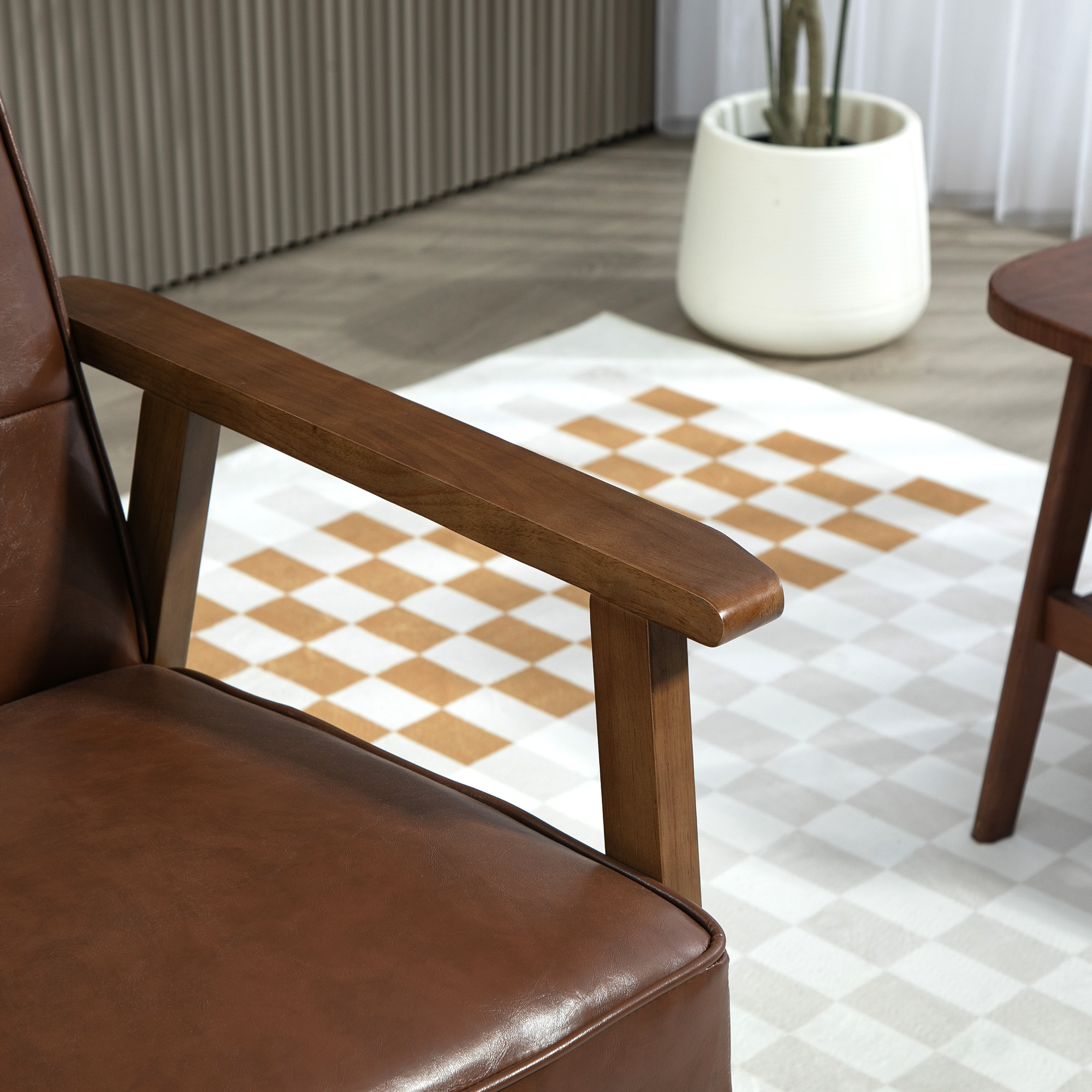 Sillón de cuero marrón con reposabrazos de madera. Alfombra a cuadros blanca y marrón. Maceta blanca en el fondo.