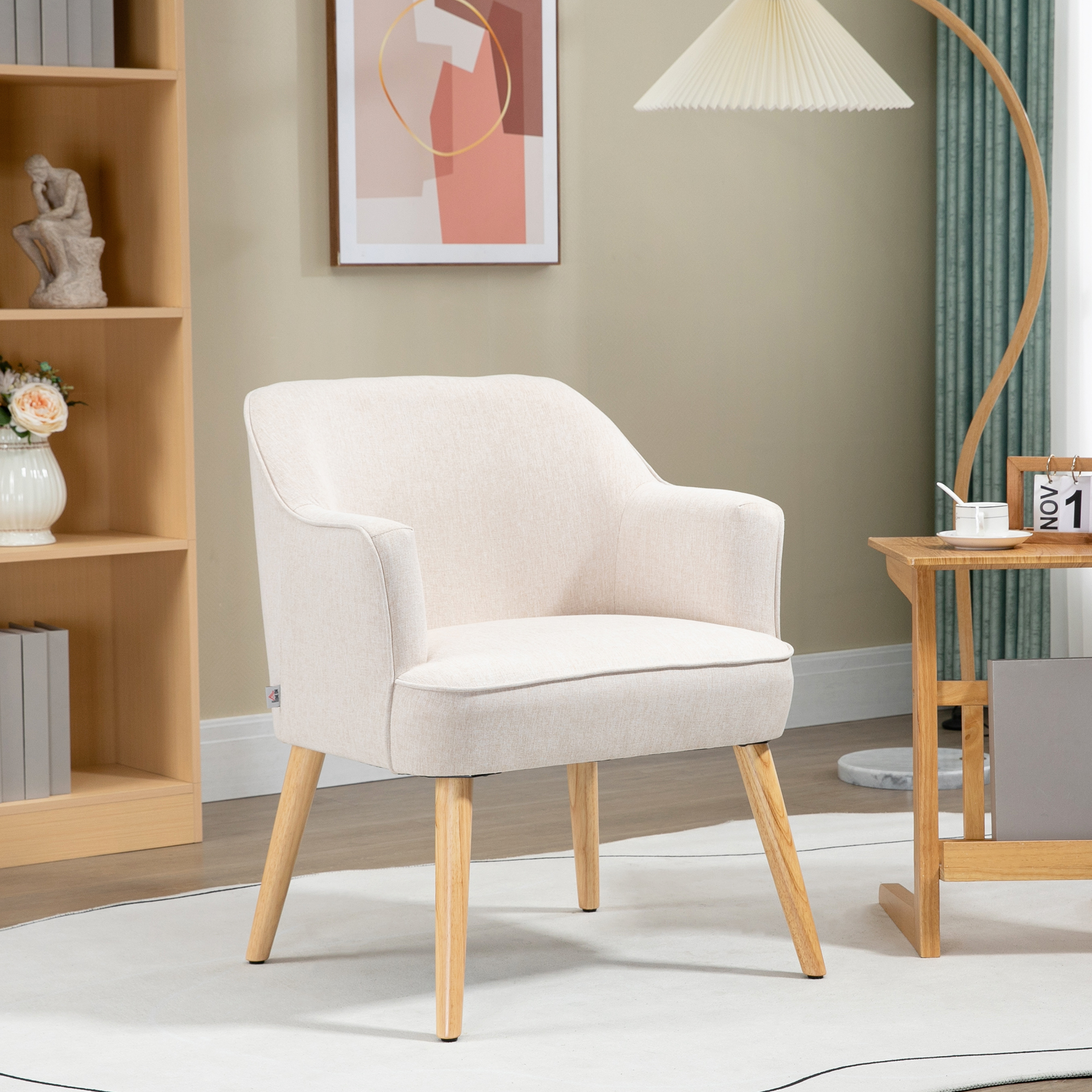 Un sillón crema con patas de madera está en una habitación. También hay una lámpara, una mesa auxiliar y una estantería.