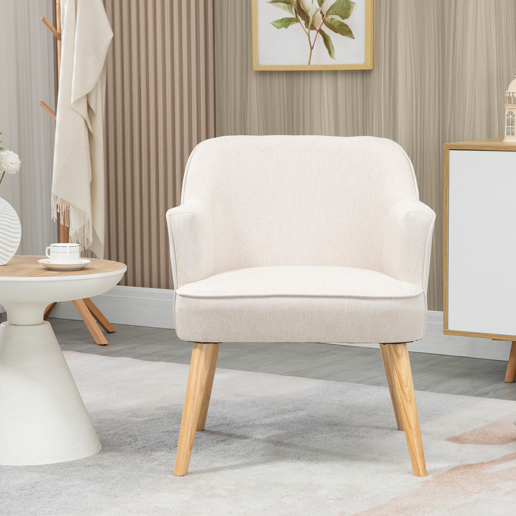 Un sillón color crema con patas de madera está en una habitación. También se ve una mesa con una taza, un armario y arte mural.